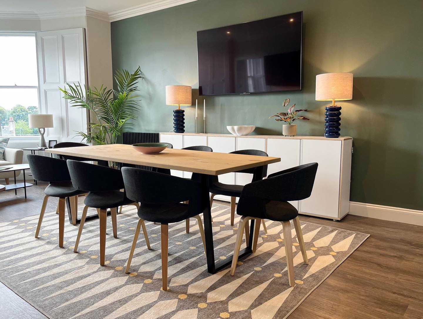 Kitchen / Dining Before & After pics - My clients love a good party so I really needed to nail the brief to make sure this would be a fun and practical space for them.
Alongside creating more storage space and worktop area, I really wanted to streamline the overall feel of the space. The large wall mounted tv felt very prominent in the room so we painted the wall in a lovely dark green to help minimise the visual impact. The sideboard underneath and table lamps either side provide some balance and symmetry. The lower-level lighting also creates a lovely atmosphere in the evening when the overhead lighting is turned off, perfect for entertaining.
Introducing a large rug (washable) under the dining table has really helped with the acoustics whilst the pattern injects a little energy.
I hope this provides the perfect setting for many memorable party nights in the future 🕺🏻🪩