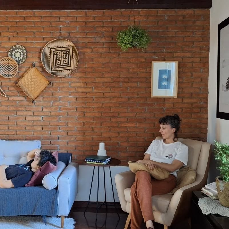 Esse é um post pra lembrar que esse perfil não produz conteúdo com frequência, que o estilo digital por aqui é o tal do low-profile (aceito dicas de termos em português, há de ter algum melhor que esse).
Por aqui as publicações aparecem só quando tempo e disposição se encontram.
Então, a meta não é gerar conteúdo infinito com conselhos que ninguém pediu. As ideias de postagem vem da rotina de atendimentos, despertadas pelos corpos-mentes que chegam até mim e, ás vezes, viram post.
Achei importante contar que o conteúdo que chega aqui transita antes, na vida real. Não porque alguém me cobrou, mas quando se tem uma página nessa plataforma parece que a pressão de postar acompanha.
Tem grupo terapêutico acontecendo, tem agenda de atendimentos presenciais e on-line acontecendo, tem vida pessoal acontecendo e tem desejo de espaço vazio. Afinal, a vida também acontece na brecha. (essa é fala de uma das pessoas que atendo).
Na foto se vê nossa sala de atendimento presencial. Brunella experimenta a poltrona nova e eu incorporo a paciente no divã. A gente não pode se atender, obviamente. Mas a gente se cuida muito.
Se você chegou recente por aqui, bem-vinda. Desejo que desfrute do conteúdo que já existe e dos poucos - porém com muito amor e dedicação - que ainda virão.