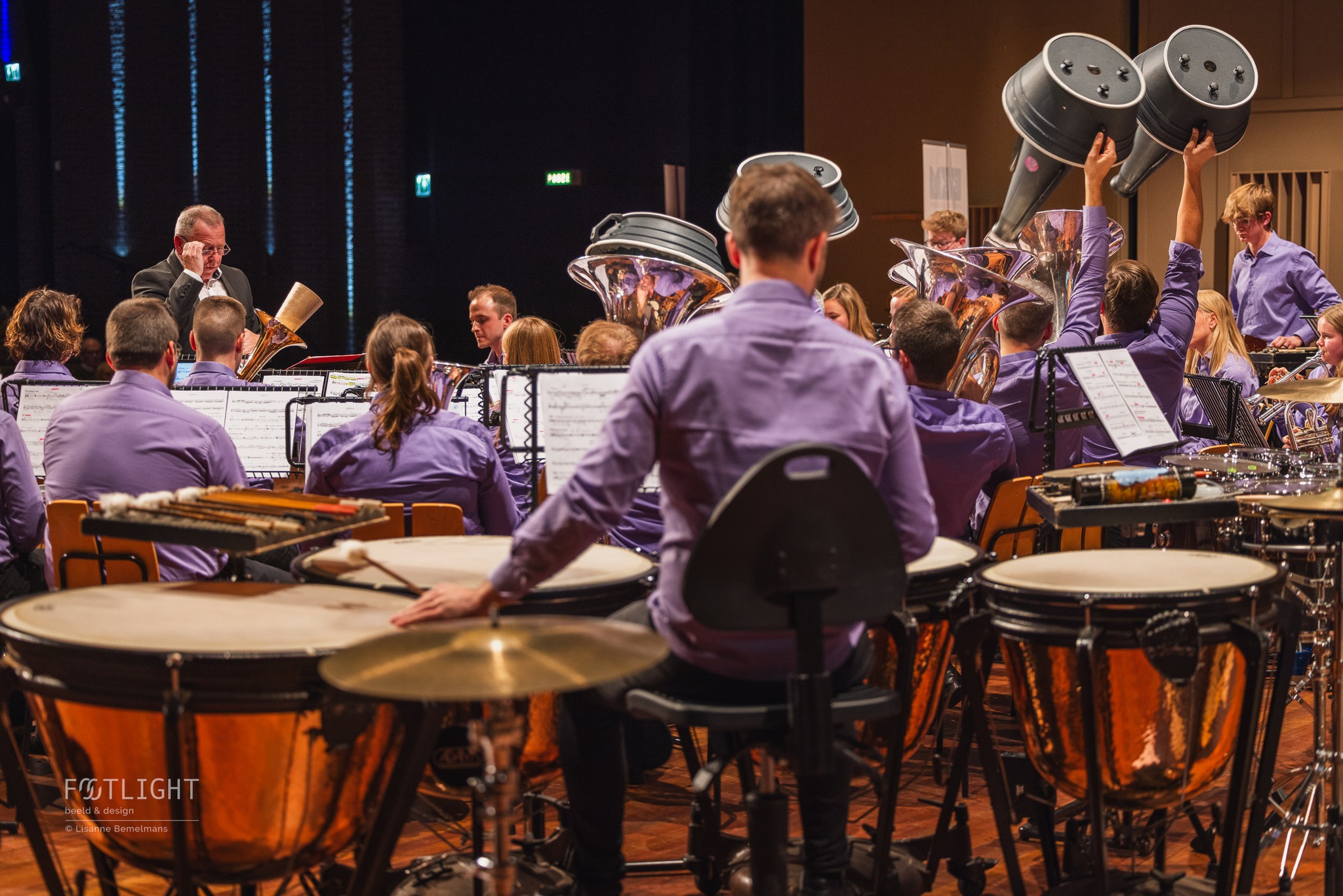 Ik hoopte maar dat de houten theater vloer niet te hard ging kraken. Ik moest hoe dan ook het perfecte plaatje schieten. Vanuit de zaal had ik mijn eerste foto’s en ik vroeg mij af: ‘Wat kunnen de mensen vanuit de zaal niet zien?’ Ik ging stilletjes backstage en mijn zoektocht ging verder.
Het orkest speelde net een zachte passage. Backstage liep ik op mijn tenen naar de andere kant. Ik hoopte dat de houten theater vloer niet te hard ging kraken en dat ik op tijd was om nieuwe momenten te vangen met mijn lens. Ik zag mijn kans tussen de decor elementen door.
Een prachtige compositie waar muzikanten een mega grote demper uit hun instrument haalde. Dan vang je een tof moment! Welk moment beschrijft voor jou een muzikale avond?
Joske Hanssen van WMC Kerkrade, was in ieder geval heel blij met de fotoserie.
#concertfotografie #concerts #musicians