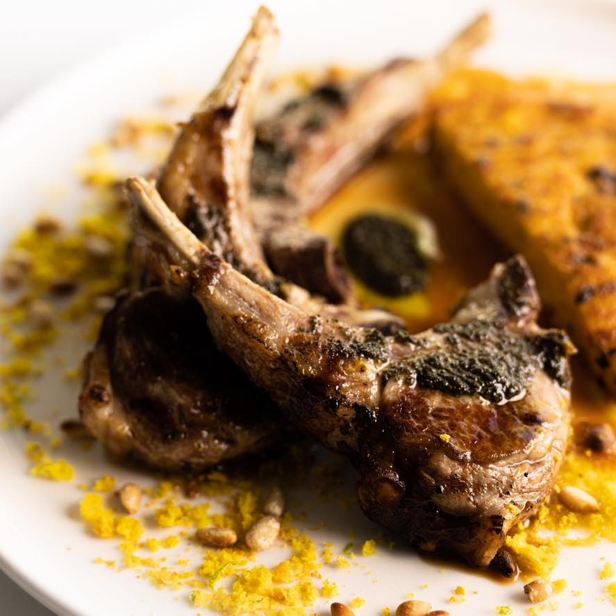 Gros plan sur nos côtelettes d’agneau grillées, gremolata aux herbes, pignons toastés, polenta croustillante aux olives, romarin et poivre noir 🐑🫒