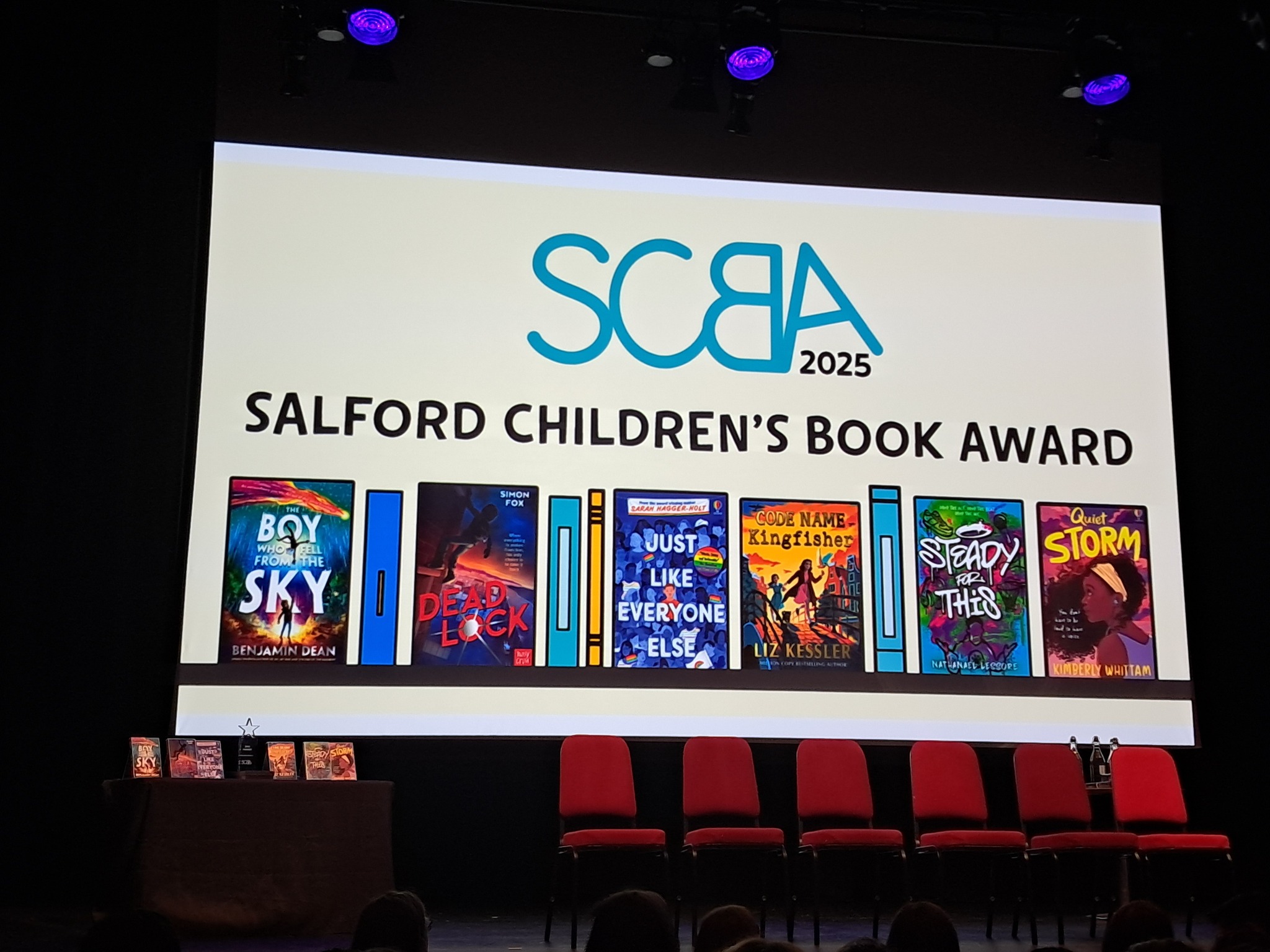 Local author Kimberley Whittam was voted this year's winner of the Salford Children's Book Award for her debut novel Quiet Storm at the ceremony held on 24th June at Salford University.
Our students joined the other 10 secondary schools taking part in the program and were in the audience to hear the shortlisted authors speak about the inspiration behind each story and their different experiences of being a writer. The event was compered expertly by children's author James Campbell who carried out this role with great enthusiasm and humour, but even amongst all the frivolity he managed to impart some impactful words of wisdom about the importance of reading and writing and the key role that libraries play in society.
Our pupils got to choose a book for themselves to keep from the book shop at the event and they were able to have their books signed by the authors. Many of our pupils took selfies with the authors as well as collecting their autographs and came back to school absolutely fizzing with excitement about the whole morning.
The fact that Kimberley won this award is even more exciting for our school as we are due to welcome her for a visit to St Ambrose this week. Pupils who would like to take part in next year's Salford Children's Book Award can speak to Mrs Davis about joining the group when it starts back up in January.
#lovelearnlead #putstambrose1st #salfordchildrensbookaward