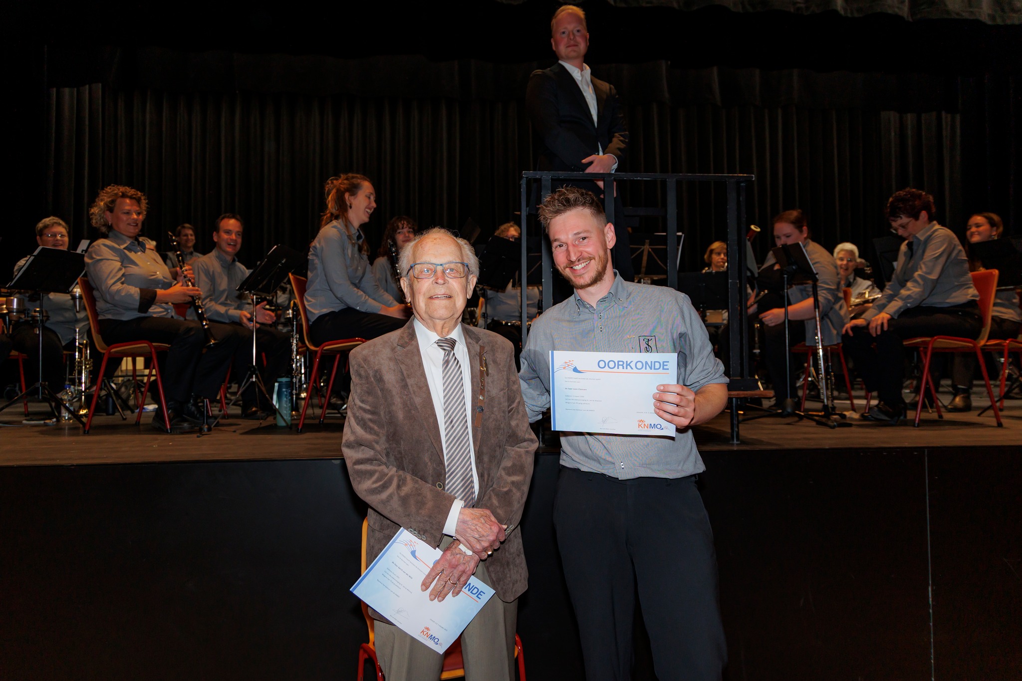 ST. JAN HULDIGT JUBILARISSEN
Leon Claassen en Gerrit van de Wiel samen 100 jaar lid.
Afgelopen zondag was een bijzondere dag voor Muziekvereniging ‘St. Jan’. Tijdens een goed bezocht Jubilarissenconcert in ,’t Wapen van Wanroij’ werden twee leden van de vereniging in het zonnetje gezet.
Nadat de slagwerkgroep onder leiding van Anthony Vogels van zich had laten horen met een gevarieerd en uitdagend repertoire en de harmonie onder leiding van Dennis Frenken ook de eerste muziekstukken ten gehore had gebracht, was het slagwerker Leon Claassen die als eerste in de schijnwerpers werd gezet. Leon is 25 jaar lid van Muziekvereniging ‘St. Jan’ en werd door de heer Robert Verhofstad als afgevaardigde van de Brabantse Bond van Muziekverenigingen gedecoreerd met een zilveren speld.
Maar met 25 jaar lidmaatschap komt Leon nog maar net kijken in vergelijking met de andere jubilaris: Gerrit van de Wiel. Gerrit werd in 1950 lid van toen nog Kerkelijke Fanfare ‘St. Jan’ en is hiermee al 75 jaar verbonden aan de vereniging. Een unicum voor ‘St. Jan’. Het Jubilarissenconcert werd dan ook in het bijzonder aangeboden aan Gerrit, zijn echtgenote Hanny en familie.
Tot op hoge leeftijd heeft Gerrit de hoorn bespeeld. Nog steeds is Gerrit bijna iedere maandag op de repetitie aanwezig om te luisteren en een kopje koffie mee te drinken, iets waar hij zelf jarenlang in de pauzes voor heeft gezorgd. Het was dan ook een grote eer om Gerrit te mogen onderscheiden met de bronzen bondsmedaille voor dit bijzondere jubileum.
Met nog enkele spectaculaire muziekstukken sloot het harmonieorkest na de huldiging het concert af. Tevens presenteerde de muziekvereniging deze dag nieuwe, moderne, zwarte jassen, waarmee na vele jaren afscheid wordt genomen van de bekende bordeauxrode uniformjassen. Met de jubilarissen in het midden werd dan ook met trots een nieuwe groepsfoto gemaakt van Muziekvereniging ‘St. Jan’.