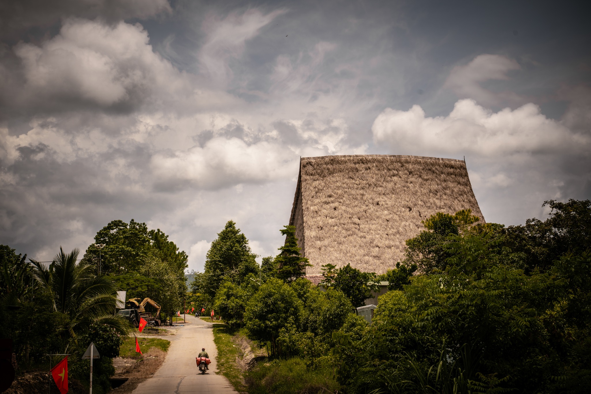 The Nhà Rông, these great communal houses of Vietnam’s Central Highlands, rise proudly at the heart of Bahnar and Jrai villages.
Each village has its own, its roof lifting higher with the number of inhabitants. Majestic, it takes on many meanings: some see the shape of an axe, others a sail — a memory of the ocean carried by Austronesian peoples who once journeyed here from Taiwan and the Philippines.
But what moves me most is that they are still alive.
Here, tradition is not frozen in time: the Nhà Rông are still built, still lived in, still filled with laughter and conversation. They remain the symbolic and social heart of the village — a place for rituals, celebrations, and collective decisions, the pulse of community life.
And yet, they evolve.
Outside, a volleyball court. Inside, television and wifi share space with ethnic ornaments.
Young men sleep there, children play beneath the beams.
Customs shift, culture breathes — but the spirit endures.
Here, tradition is no relic.
Here, architecture is alive.