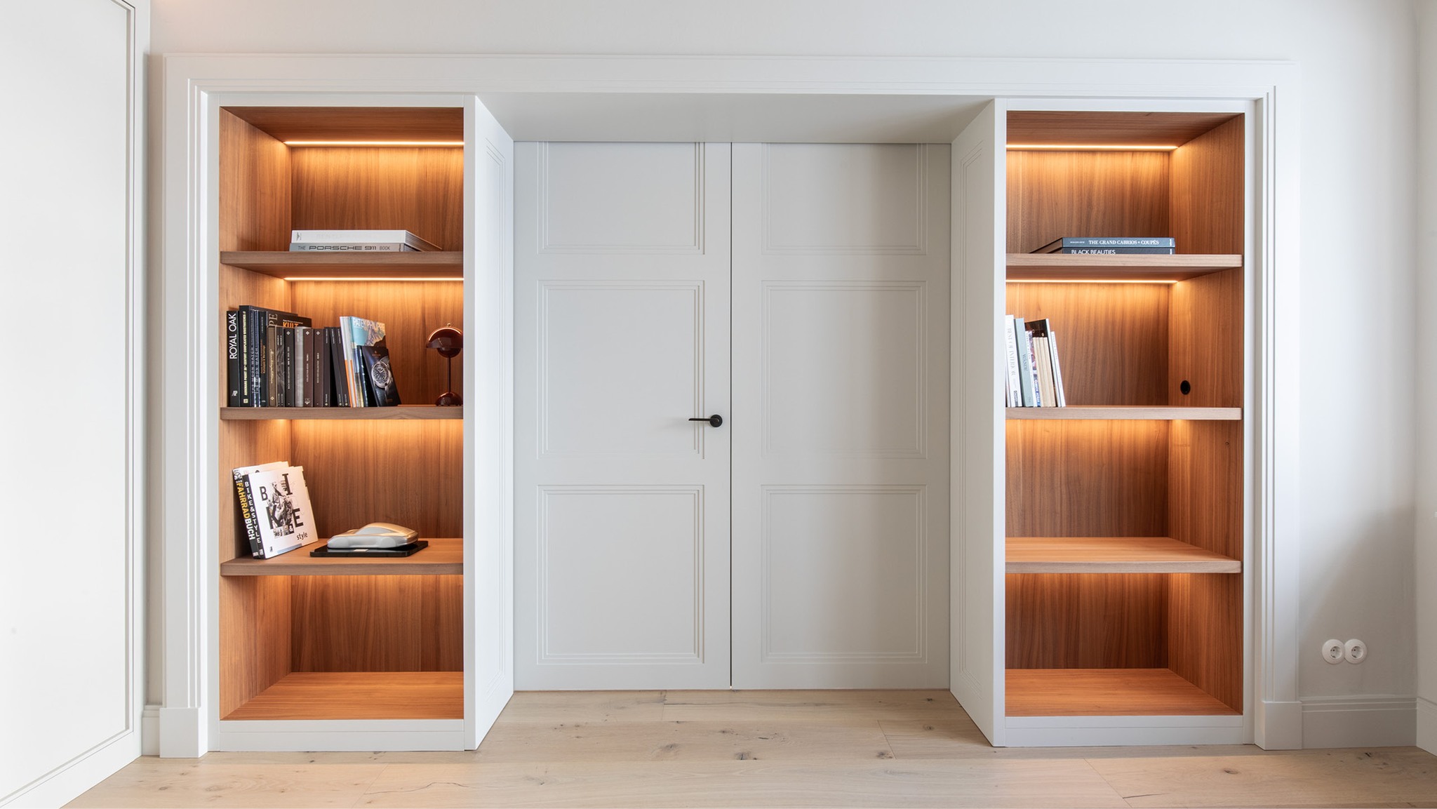 Kontrastvoll komponiert. Lackierte (Weiße) Flächen treffen auf die Nussbaum (Tiefe dunkler Eiche). Die weißen Flügeltüren mit filigranen Holzprofilen werden beidseitig von maßgefertigten Regalen eingefasst. Deren integrierte LED-Beleuchtung inszeniert das Zusammenspiel von Licht, Material und Form – und schafft eine warme, zurückhaltende Eleganz.
#interiordesign #fluegeltuer #moebeldesign #ledlight #massgefertigt