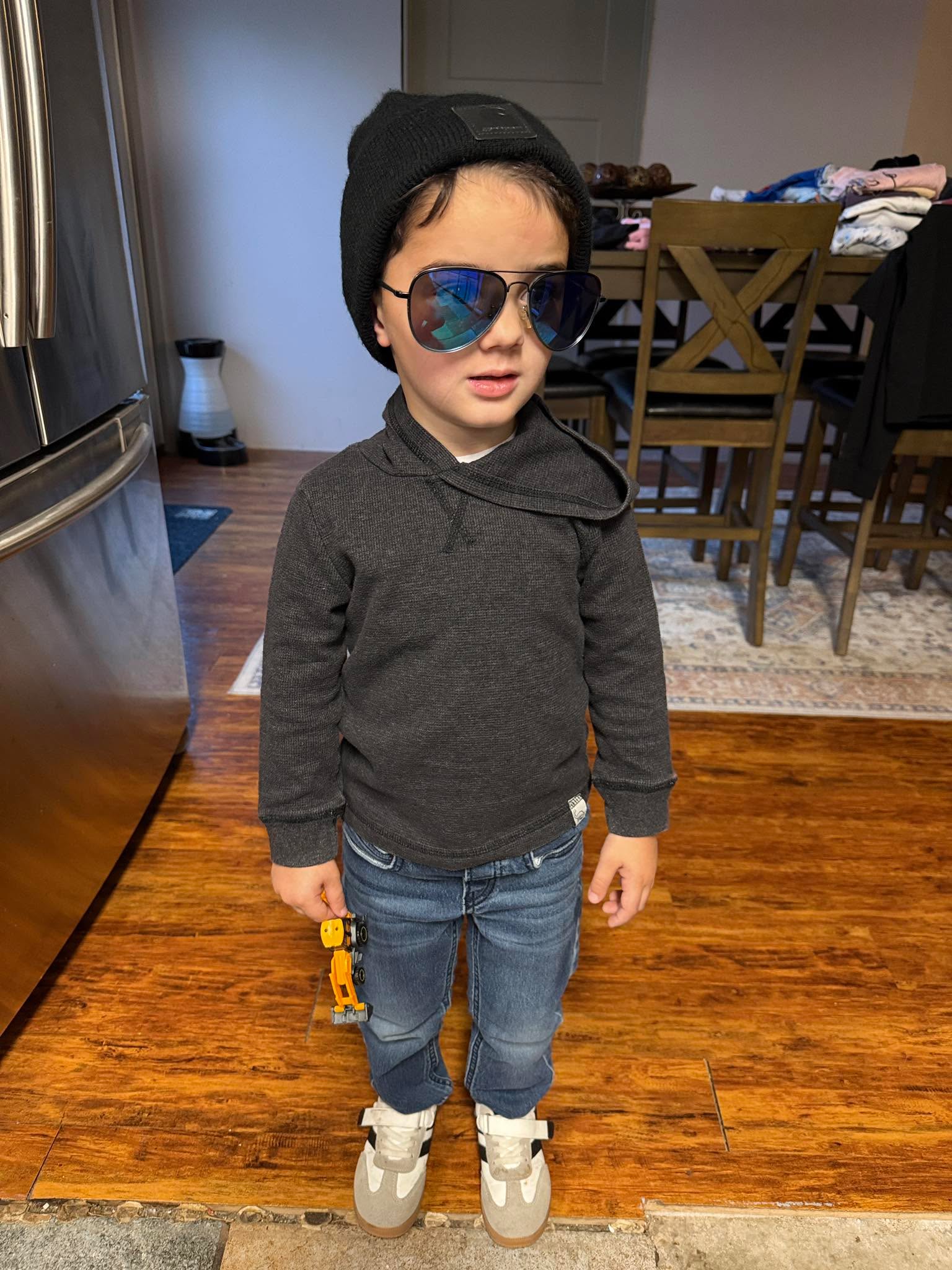 This kid walked out of his room this morning like he just dropped a platinum album and had a meeting with his agent.
Beanie? Check. Shades? Check. Construction vehicle in hand? Check.
Johnny’s got that effortless cool that can’t be taught…just inherited.