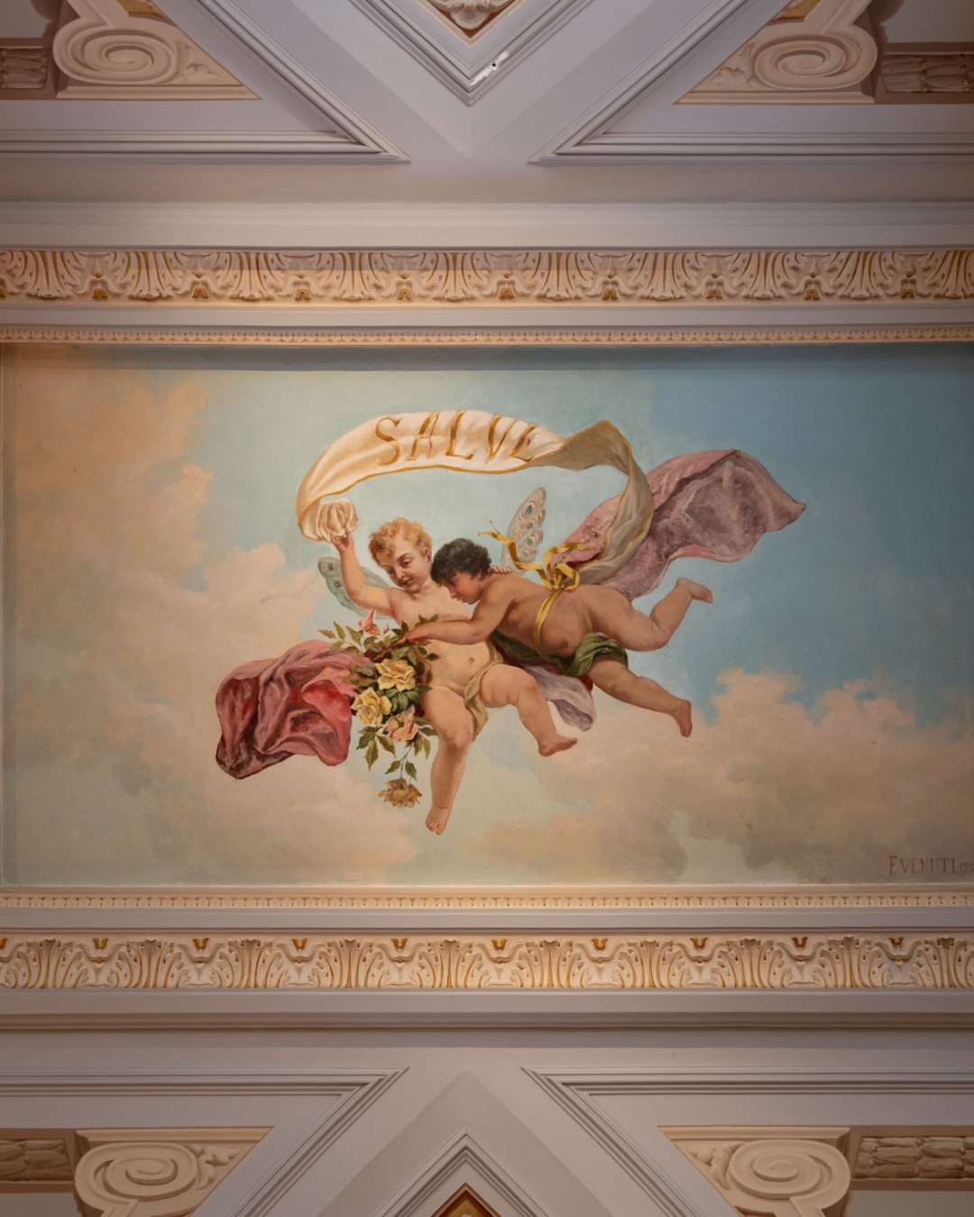 Most greetings are found underfoot - a welcome mat, perhaps, or words inlaid in marble, like at the Dragonara Palace, built by Giuseppe Scicluna's uncle. But Giuseppe had other ideas.
When he commissioned Filippo Venuti to paint the entrance ceiling in 1901, he placed his greeting in the sky instead: "Salve," held aloft by two cherubic putti who've been welcoming guests for over a century. It's a small rebellion, this insistence on looking up rather than down when you arrive. One of many quiet nods to the Dragonara Palace that you'll find tucked throughout these rooms. Next time you visit, look for them.
#PalazzoParisio #PalaceLife #visitpalazzoparisio #palazzoparisiomalta #palazzoparisionaxxar