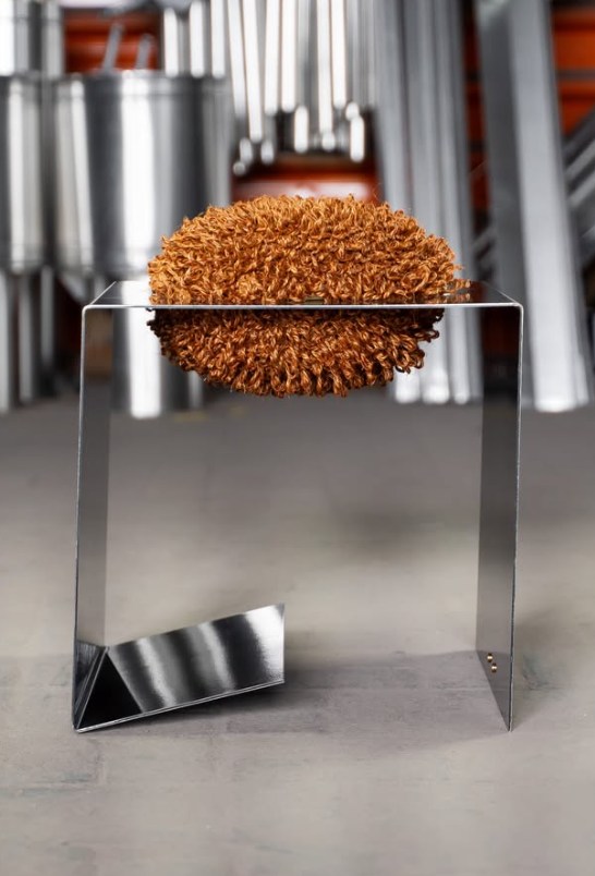 Na Impermanência 2026, recebemos o La Poltrona Studio (@lapoltronastudio), estúdio fundado por Pamela Cantelmi, artista e designer argentina que vive no sul do Brasil desde 2015.
Sediado em Imbituba (SC), o estúdio desenvolve peças que exploram o encontro entre materiais naturais e processos artesanais. Fibras como sisal, rami, palha de bananeira e buriti aparecem com frequência em seus projetos, sempre trabalhadas manualmente.
A peça apresentada, Banco Petra, parte de uma estrutura metálica criada a partir do reaproveitamento de componentes descartados, preservando a força estrutural e a memória do material.
Sobre essa base, o sisal tricotado manualmente em bucles introduz movimento e irregularidade, criando um contraste entre a precisão do metal e a organicidade da fibra.
O resultado é um diálogo entre indústria e artesanato, onde cada peça se torna única a partir das formas e curvas da estrutura reaproveitada. @lapoltronastudio