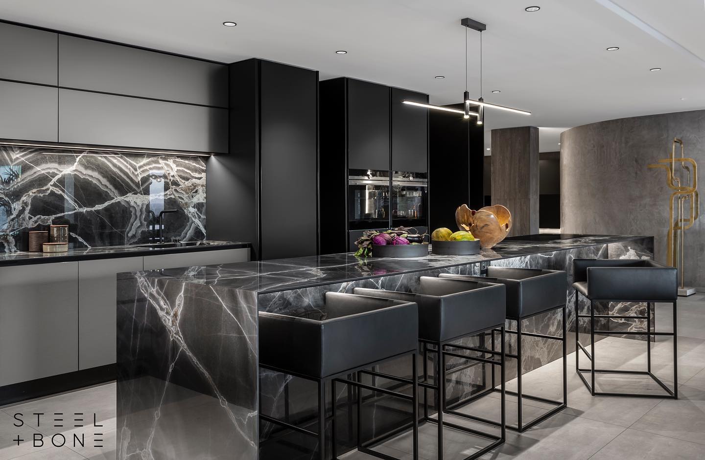 MAJESTIC ONYX MAGIC
Another premium production and display of artisan perfection, here we bring you the final photos of a breathtaking project undertaken in collaboration with Steel & Bone Official.
Featuring fully cladded surfaces on the walls, splash back, kitchen island and a custom integrated sink, our team at Rock & Stone fabricated and installed all of the above stonework using 6mm Majestic Onyx by Fiandré Maximum Surfaces.
Majestic Onyx encapsulates the beauty of European luxury and designer trendiness. The 3D depth and movement of this stone is a spectacular sight to behold with it’s dramatic marble effect displaying a variation of deep, charcoal black hues and smokey veining depicting the banded, layered mineral depositions well known in Onyx stone.
Majestic Onyx boasts a strong artistic display which is best suited for accent pieces or high end interiors, whether used in darker themed interior designs or areas where powerful contrasts are to be created. The visual aesthetic of this highly detailed stone is invigorating, mystical and enchanting with lighter veining flowing throughout the slab from thin to thick, merging to create moments of dramatic contrast and colour variation against a bold, black base.
Majestic Onyx is beautifully complimented by the moody, dark joinery, furniture and accents in this interior.
At Rock & Stone we love to push the boundaries of craftsmanship through unique, challenging designs which require precision work and a detailed eye.
It’s nothing short of an honour to collaborate on projects such as this with some of the best in the business and we look forward to many more.
Well done to all involved in creating this masterpiece.
Designed by @steelandboneofficial
Stonework by @rockandstoneworks
Material by @studiomasson.capetown
Glasswork by @glass_benders
Photos by @niel_vos_photography