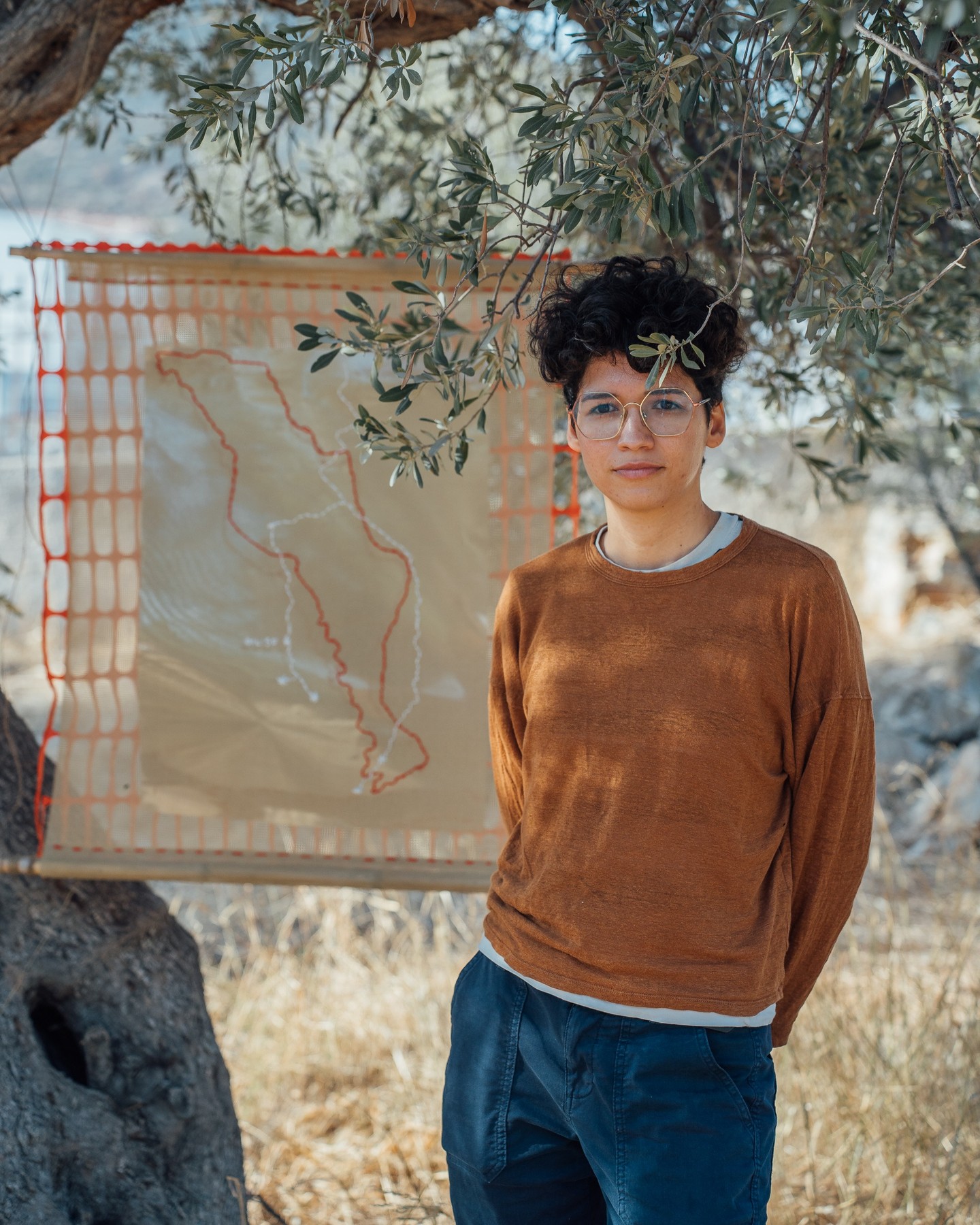 This project offers a layered portrait of the area surrounding Villa M in Evia through diverse mappings created locally—using photos, walks, explorations, and interactions with the community. In an era where maps and narratives are often shaped by political and economic interests, this project asks: Can a counter-artifact—a map designed to defy rather than define—become a material and conceptual tool for political subversion?
This counter-mapping project seeks to challenge hegemonic narratives by integrating political, geographical, and social perspectives that reveal more than what’s typically dictated from above. Through the zine, the project resists linear storytelling, allowing multiple entry points and opening an "archive of escape" that invites readers to chart their own interpretations. The installation, too, embodies this approach. Featuring an inverted embroidered map of Evia suspended on translucent fabric before a mirror, it draws viewers into the work—placing their reflections within the map and emphasizing that territory and presence are intertwined and in constant flux.
This work does not aim to define distances but rather to deepen the meanings and relationships we create within them. By blending the physicality of the installation with the open, fragmented format of the zine, the project invites viewers to explore and reinterpret their connections to place, memory, and identity—proposing mapping as an act of exploration, reimagination, and collective subversion.
Berenice Zambrano (Graphic Designer)
Berenice Zambrano is curious about what other possibilities are possible while focusing on the political aspects of collective experiences. She draws inspiration from Oaxaca, cycling, and music genres like techno, ambient, and cumbia, as well as from artists such as Isaura Leonardo, Yásnaya E. Gil, Alf Bojórquez, Javier Raya, and Brenda Navarro. Engaging in various projects, she addresses socio-political issues from creative and cultural perspectives. In her work, she uses counter-artifacts as tools to question and propose different ways of being, knowing, doing, and relating, while exploring the space between the real and the possible.