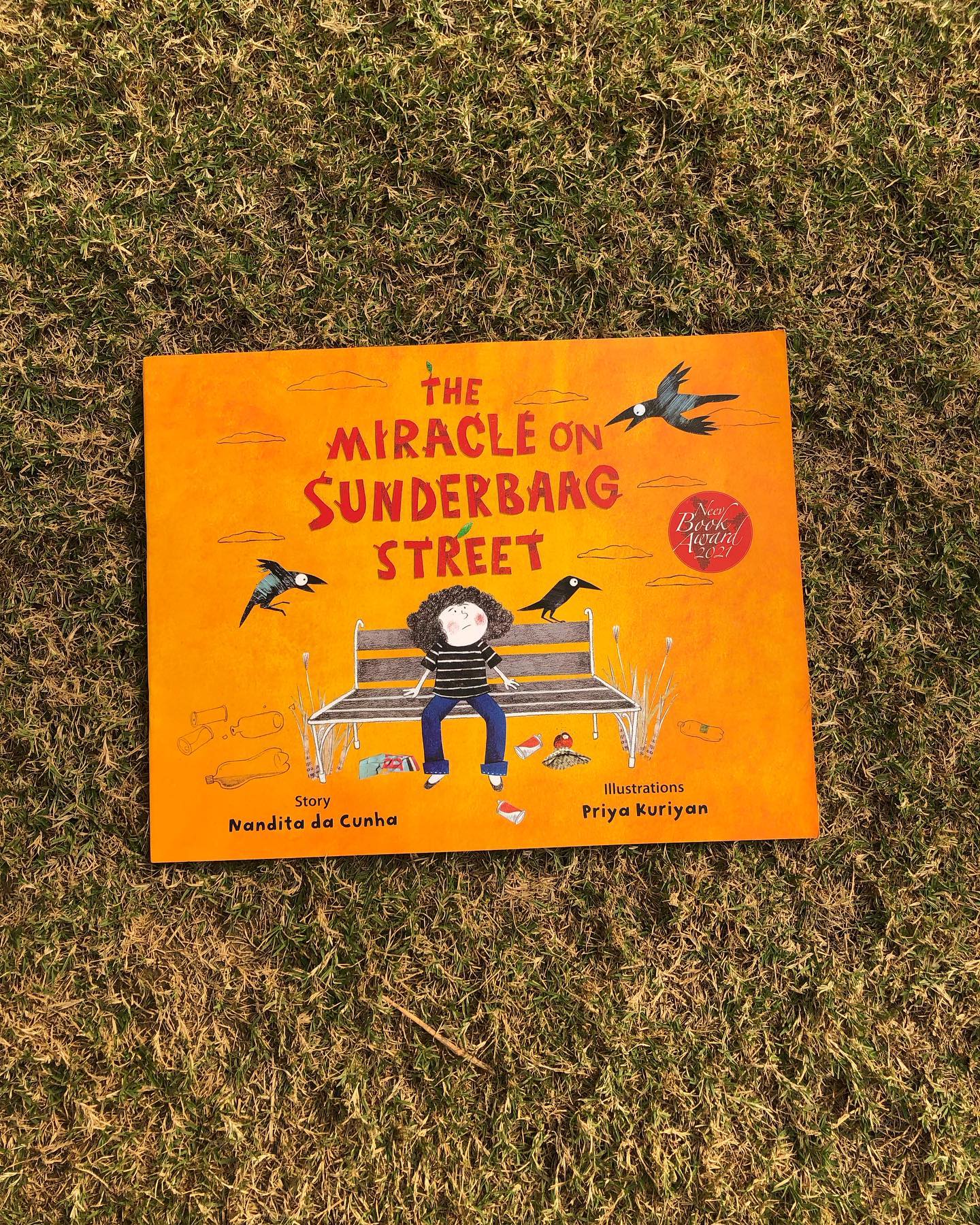 The Miracle on Sunderbaag Street
By Nandita da Cunha
Illustrated by Priya Kuriyan
Having loved The Miracle on Kachua Beach, we were eager to read The Miracle on Sunderbaag Street, especially given the glowing reviews it has received—and it did not disappoint. This beautifully crafted story sensitively addresses themes of loss and healing, while highlighting the profound connection between nature and human resilience.
The story follows Zara, a young girl grappling with deep loss that has left her withdrawn. Her favorite retreat is a neglected, decrepit dumpyard—an unlikely sanctuary frequented by no one except a group of boys practicing their not-so-melodious tunes and her old craft teacher, Miss Gappi. Known for her endless chatter, Miss Gappi initially irritates Zara, who prefers solitude. However, Zara’s curiosity is piqued by Miss Gappi’s activities and her captivating stories.
Interwoven into the narrative is the dumpyard’s history—once a vibrant, flourishing garden beloved by the community. Inspired by this tale and Miss Gappi’s gentle guidance, Zara finds a renewed sense of purpose. In her journey of healing, she not only transforms her own life but also breathes new life into the community, turning the desolate dumpyard into a space of collective joy and inspiration.
In a world where children often feel insulated from the bigger picture, this story serves as a poignant reminder that even small acts of care can lead to profound change. It beautifully conveys the message that anyone, no matter how young, can be a catalyst for transformation.
Sensitive, uplifting, and thought-provoking, The Miracle on Sunderbaag Street is a must-read for children aged 6 and above.