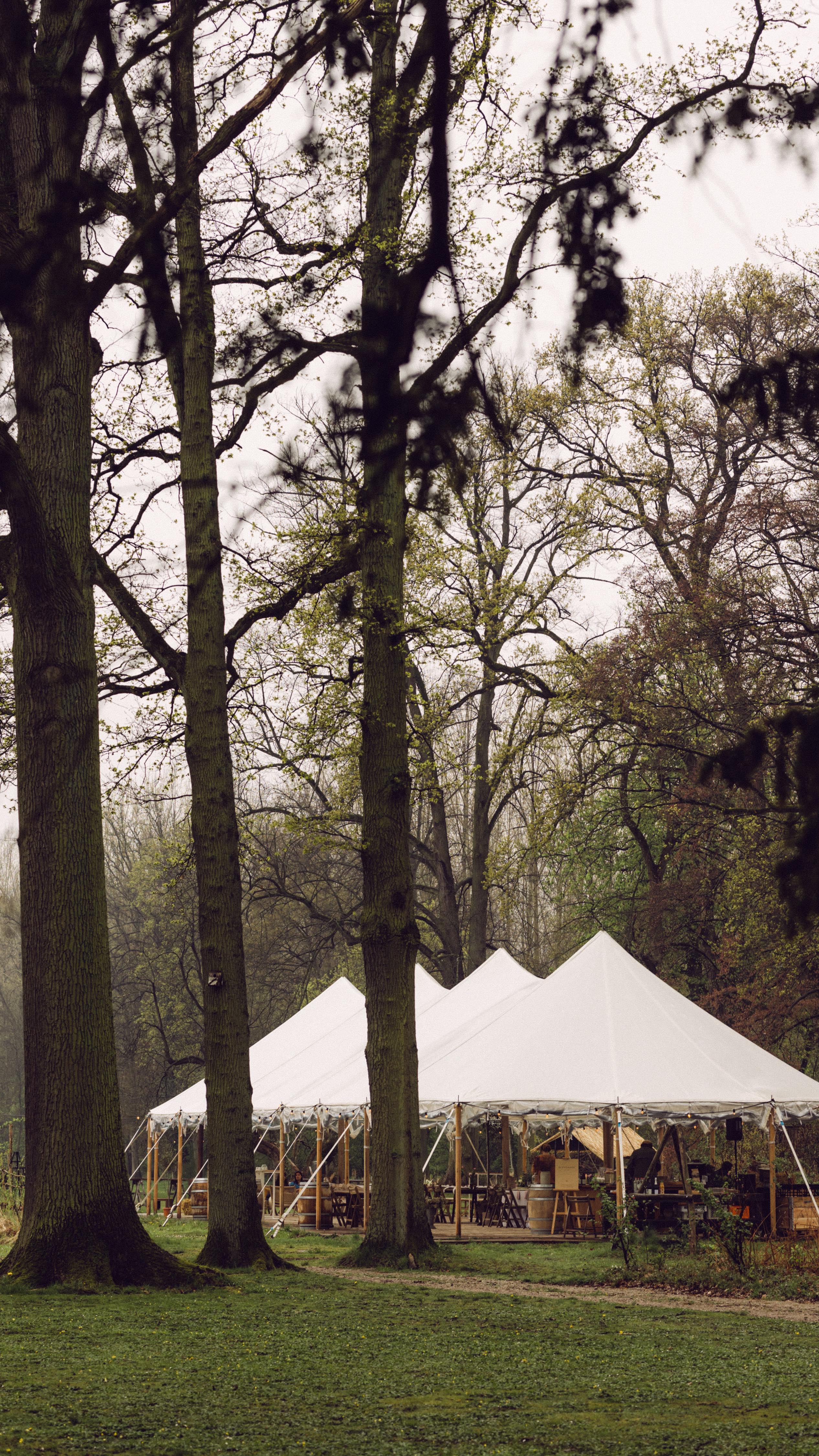 Een grote tent kan niet zomaar eender waar geplaatst worden. Een paar aandachtspunten als je een geschikte locatie zoekt voor je tenthuwelijk:
1. Er moet uiteraard ruimte genoeg zijn om de tentoppervlakte te creëren die je nodig hebt. Hoeveel dat precies is, hangt af van wat er allemaal in de tent moet komen, maar doorgaans reken je 1,5 tot 2 vierkante meter per persoon.
2. Hou er daarnaast rekening mee dat er ook nog ankerpunten voor de tent in de grond moeten worden vastgemaakt. Je hebt dus nog een paar meter extra nodig rondom de tent. Kan er niet in de grond verankerd worden, bijvoorbeeld door een stenen ondergrond, dan beschikken de meeste tentleveranciers over betonnen gewichten als verankering.
3. Kies je voor een tuin of weide, informeer dan bij de eigenaar of de ondergrond snel drassig wordt bij regenval. Sommige gebieden zijn daar gevoeliger aan dan andere en een drassige wei is allesbehalve optimaal.
5. Verder mag de ondergrond geen te grote helling hebben. Een tent, zeker eentje met vloer, wordt altijd waterpas gezet, en dus op de nodige hellende plaatsen gestut, maar er mag geen te groot hoogteverschil zijn tussen beide uiteinden van de tent om de stabiliteit (en dus veiligheid) te kunnen garanderen.
En de belangrijkste tip: laat het inschatten van het terrein over aan mensen met kennis van zaken, dus laat je tentleverancier zeker ook altijd eens ter plaatse komen voor een locatiebezoek.
Handige tips? Save for later! ✌🏻
Foto @neledaems.weddings