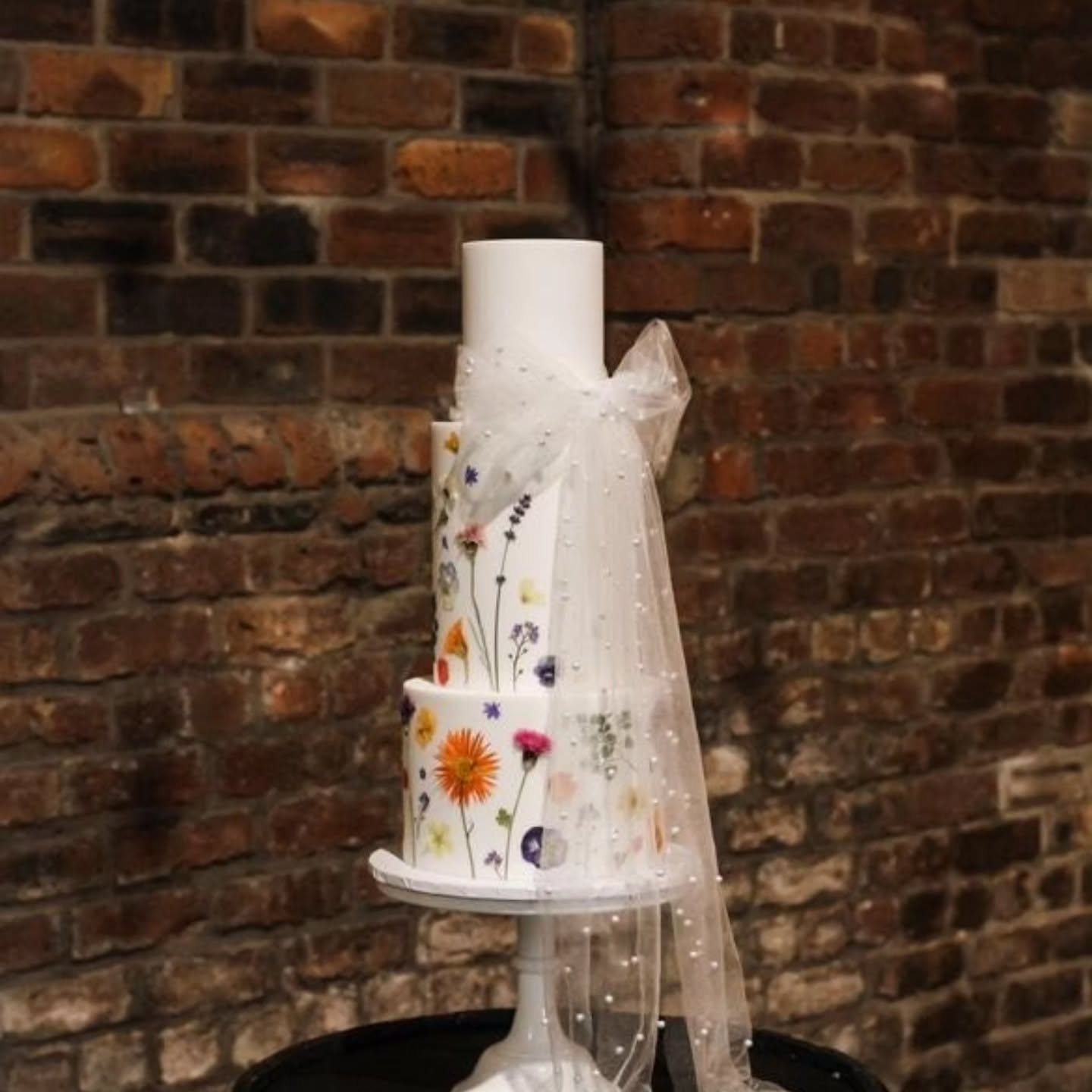 Elegance with a touch of mystery
This gorgeous cake created by @cbcakedesign has such a delicate romance. Blooms tucked gently beneath a delicate veil, peeking through like a secret garden.
#luxurycake
#weddingcakeinspiration
#bridaldetails
#natureinspired
#pressedflowers
#weddingcakes
#edibleflowers