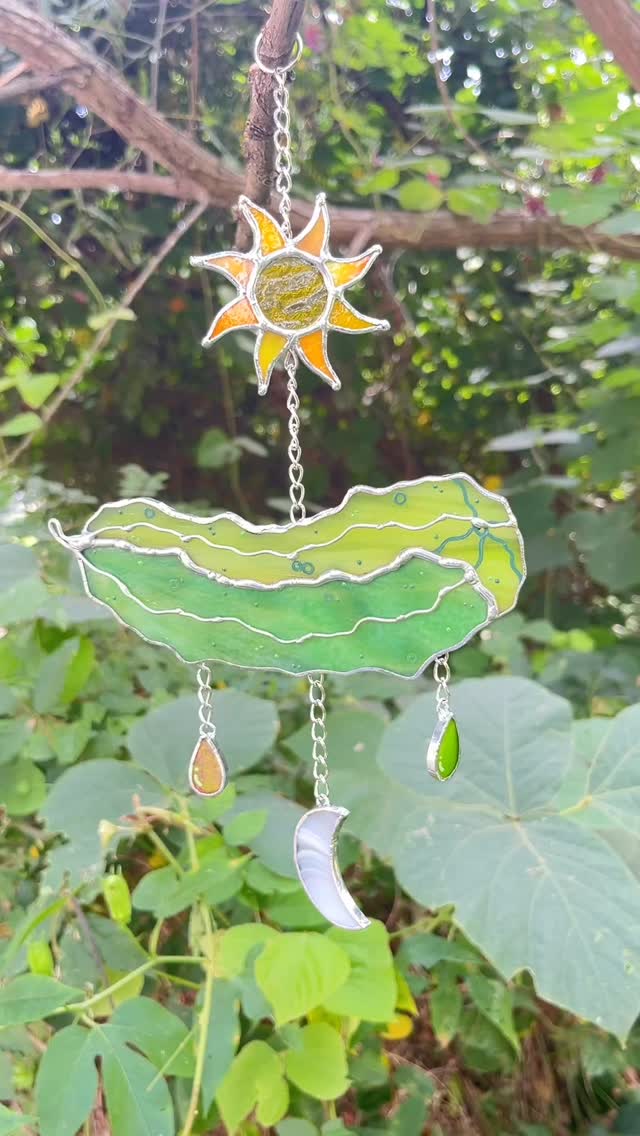 This is a unique custom we got asked to do a little while ago! ☀️🥒🌙 This customer actually sent in a little drawing of what they were envisioning - which you are always welcome to do! They also mentioned liking our methods of using small pieces, so we did every ray of the sun with a different yellow glass! 💛My only gripe? These chains are SO. HARD. to photograph! Look great resting on the window though!! If you dream it up, we’ll try and make it 💚 #stainedglassartist #stainedglassart #paigeboy #stainedglass #glassartist #pickleart #sunandmoon #queerartist #transartist