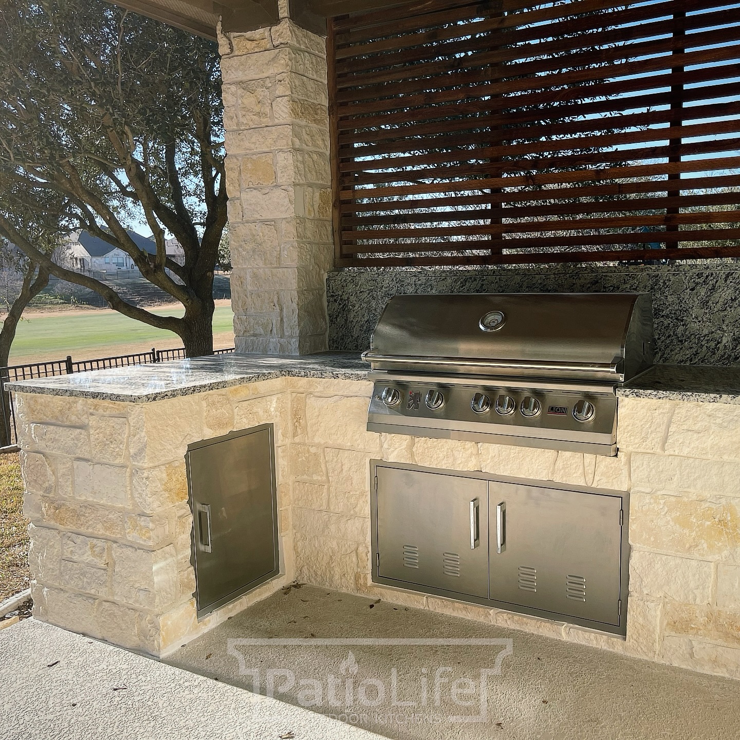 Limestone outdoor kitchen with a granite countertop, Lion grill, and a cedar privacy panel. #PatioLife