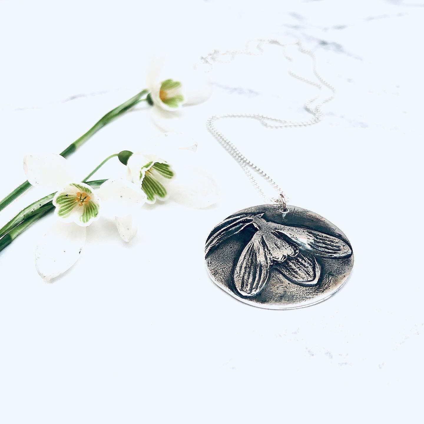 Another celebration of the humble snowdrop!
Snowdrops are a sign of hope. Of brighter times ahead. Often the first glimpse of Spring, these little joys are always a welcome sight, and spread happiness when they appear!
This handmade Silver pendant measures an impressive 3cm in diameter, and is the largest of all our ‘Botanical’ necklaces.
Check out the shop for more info x