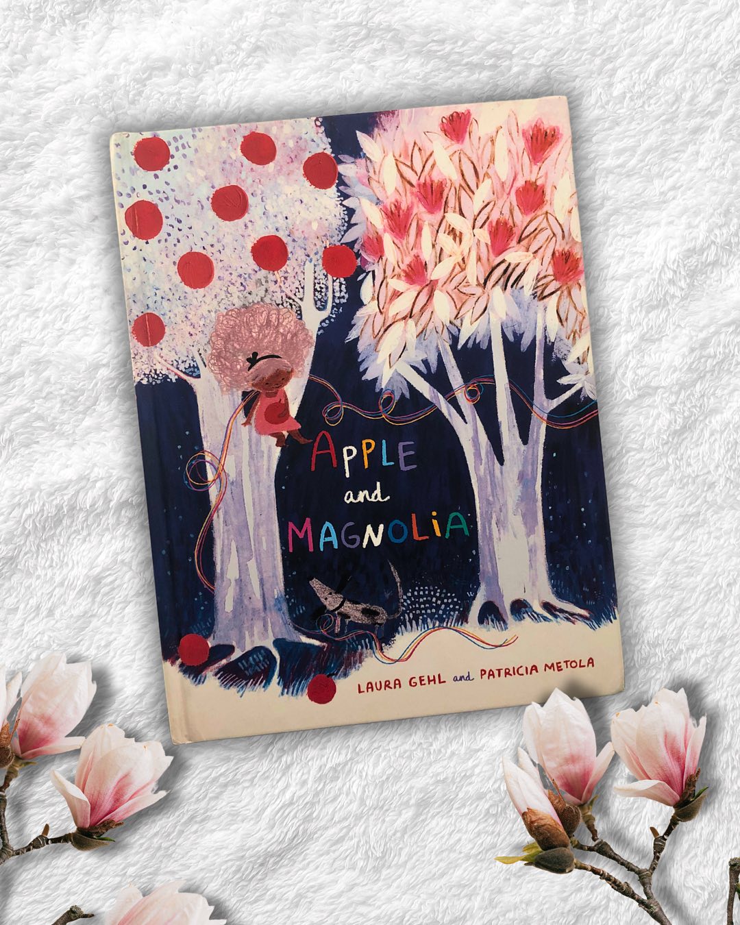 Apple and Magnolia
By Laura Gehl
Illustrated by Patricia Metola
There is so much about nature that remains a mystery, often overlooked and underappreciated. Trees, for instance, hold secrets beyond what we can comprehend. Apple and Magnolia explores this beautifully through the eyes of a young girl who wholeheartedly believes in the deep friendship between two trees—an Apple tree and a Magnolia tree.
Britta’s unwavering belief is met with skepticism. Her father gently dismisses her thoughts, and her brother outright rejects them. But her wise Nana reassures her, saying, “Unusual friendships can be the most powerful of all.” So when Magnolia begins to wither, Britta is certain that Apple can help, and she sets her heart on a plan to bring them together.
This is a tender story of love, friendship, and the boundless possibilities that come with belief. The illustrations are soft and muted, painted in an unusual yet soothing palette. Delicate, airbrushed strokes blend seamlessly with vivid bursts of color, making this book a visual delight.
A true comfort read, Apple and Magnolia never fails to uplift with its gentle storytelling and stunning artwork. Perfect for children aged 4+yrs