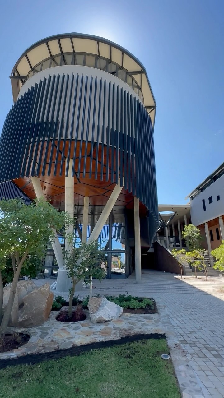 Positioned at the northern gateway to the Central Academic Core of Turfloop Campus, the new Earth Sciences Building at the University of Limpopo is designed to support the expanding Earth Sciences disciplines, providing state-of-the-art laboratories, classrooms, study spaces, and offices. Spanning 4,739m², the building adopts an H-shaped configuration, with two north-south oriented wings separated by a cascading covered external stairway that seamlessly connects all three levels and doubling up as an external amphitheatre to foster interaction and informal gatherings. The third floor of the north wing, dedicated to top-lit undergraduate laboratories, extends over three raked, double-volume lecture halls. The north façade is distinguished by a striking angular zig-zag brickwork wall, inspired by the irregular geometries of the rock samples housed within. Meanwhile, the curved western end of the laboratory floor is wrapped in Alumac aluminium profile fins, providing shading to the recessed glass façade of the canteen below. Throughout the structure, cave-like voids are carved into the façades, offering shade and respite from the intense Limpopo sun. Already a favourite among students and staff, the Earth Sciences Building has quickly become a popular gathering spot, lunch destination and a backdrop for selfies.