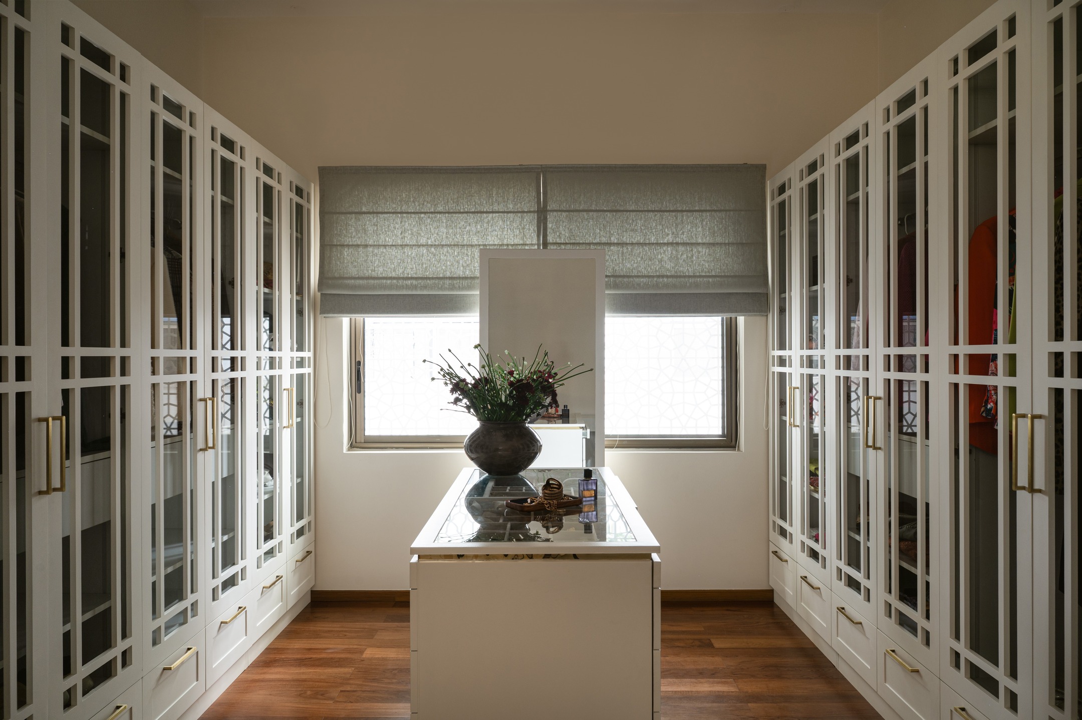 This elegant walk-in wardrobe pairs classic symmetry with modern refinement. Tall, white-framed glass cabinets showcase curated garments, accented by sleek brass hardware. A central island with a stone top grounds the space, while rich hardwood floors and a soft, patterned rug add warmth. Thoughtful detailing - like the geometric mullions — elevate this serene, light-filled dressing space into a personal gallery of style.
Design and execution : Furbishy
Photography : Nayan Soni @nayansoni21
Cinematography: Create Stories @createstories.in
Styling : Shivani Raina @theshalomhome