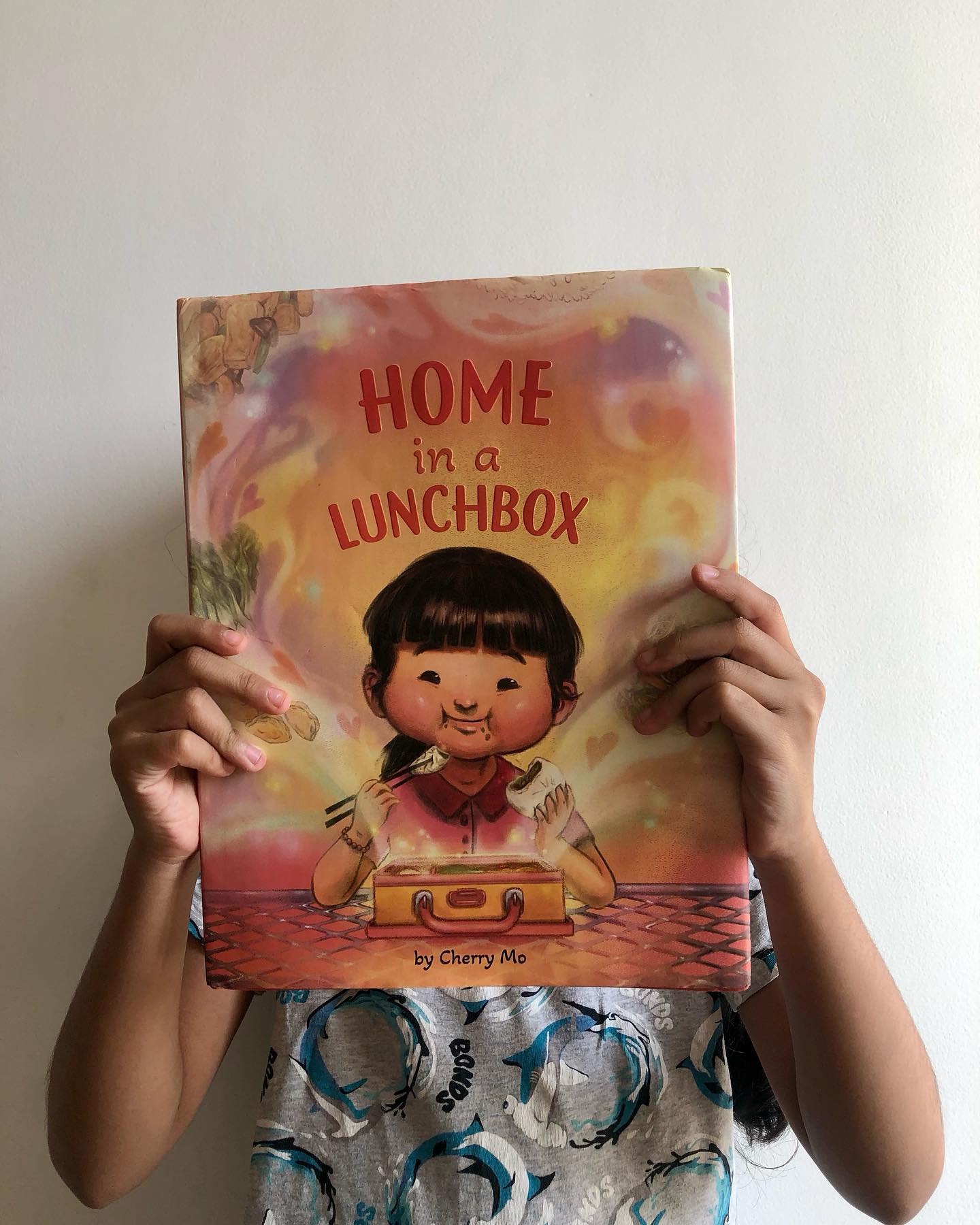 Home in a Lunchbox
By Cherry Mo
Lately, we’ve been exploring a lot of immigrant stories as a gentle way to introduce our child to the wider world - and to help make sense of what we see in the news. One theme that keeps surfacing is loneliness, something that resonates deeply with me as a parent raising a single child. It’s a feeling that quietly echoes through our own lives too.
In Home in a Lunchbox, we meet little Jun, who has just moved to America. Everything- the culture, the language, the people- feels unfamiliar. To fit in at her new school, Jun writes down English phrases on her hand with their Cantonese translations. But without any real context or support, these phrases often miss the mark, leaving her feeling even more isolated.
The one moment of comfort in Jun’s day is lunchtime. Her home-cooked meal becomes a source of joy- a warm reminder of home and her roots. These moments are beautifully brought to life through vivid illustrations filled with rainbows, hearts, and bright colors- the most visually comforting pages in the book.
At its heart, this is a story about connection. Through food, Jun begins to find common ground in her new world. And sometimes, that’s all it takes- a shared meal, a familiar flavor- to bridge differences. While the book is almost wordless, its storytelling is powerful. Jun’s emotional journey- her sadness, resilience, and quiet strength- is something we felt deeply connected to.
Ideal for children aged 3 and up.