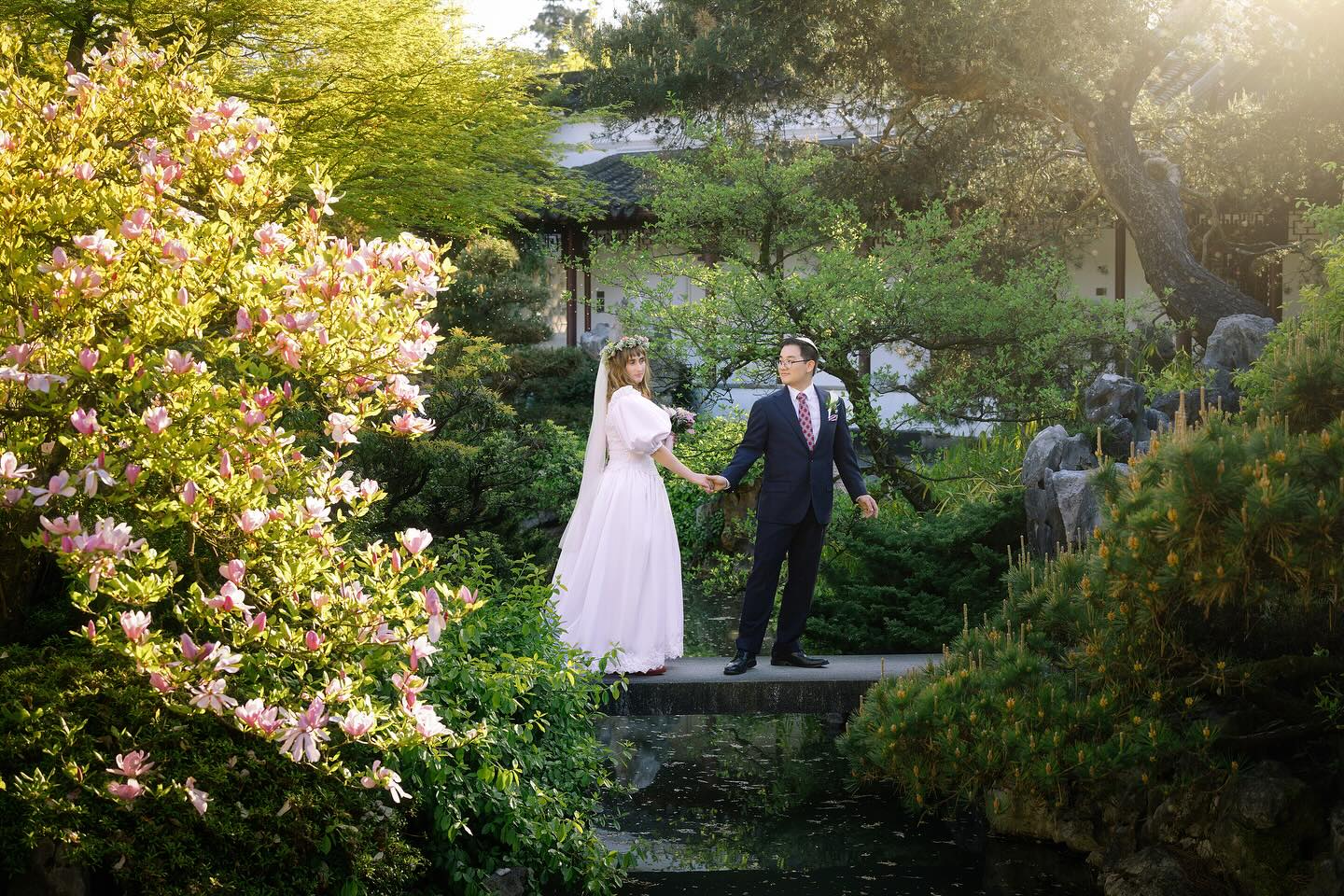 April 27th, 2025. 🪷Under the chuppah at the Chinese garden.🪷We drank Manischevtiz and plum wine. Our elders, Chinese and Filipino and Jewish came up and blessed us. Our family and friends held up the poles of our chuppah. We danced to Klezmer and sang karaoke. Kris wore a suit he had made in Manila, along with callalily pinned to his jacket and a special pomegranate kippah we ordered from Israel. I wore a dreamy pink vintage princess dress and an updated version of my mom’s wedding dress along with my great grandma’s pearls and a flower crown made by my mom that very morning. All of it was joyous, exhausting, hilarious, and just right. A celebration of union and community, culture, and faith. Blessed to be married to a fellow magic maker. ✨Ani l’dodi v’dodi li. Alterations: @gownandglove Coordinator: @eventsbybruno Photos: @tingphotography (candid at the end by my uncle:) Music: @shmalkan and @bill_piggott Officiant: Rabbi Arik from @orshalom Locations:@vancouverchinesegarden and @versantehotelcanada