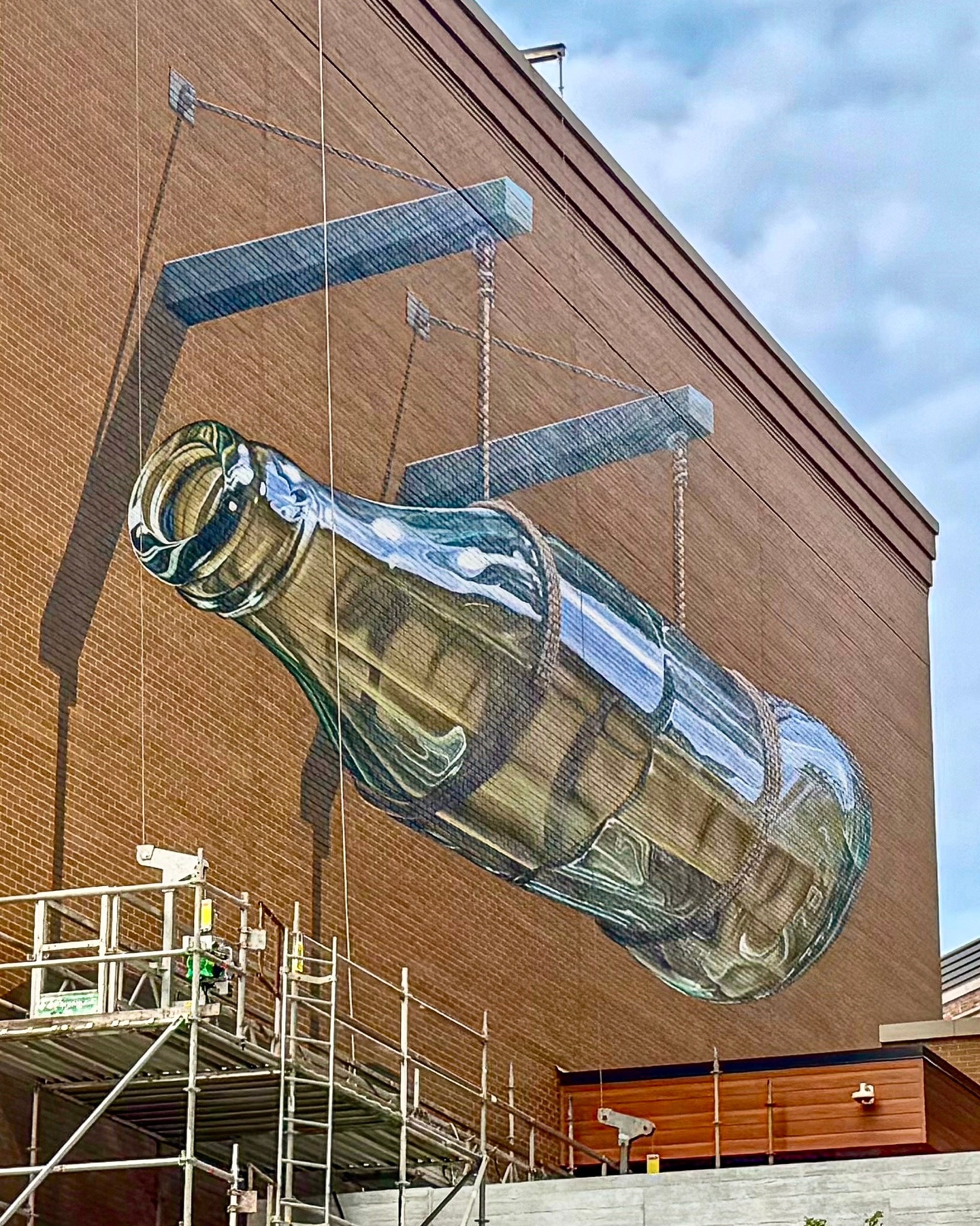 A symbol of the past, standing tall in the present.
Have you seen the latest mural at Bottleworks? This striking, larger-than-life Coca-Cola bottle pays tribute to the District’s storied past as the former Coca-Cola Bottling Plant, connecting the District’s roots to the vibrant destination it is today.
Created by artist Carl Leck, you can spot it from Mass Ave as you head north on College.