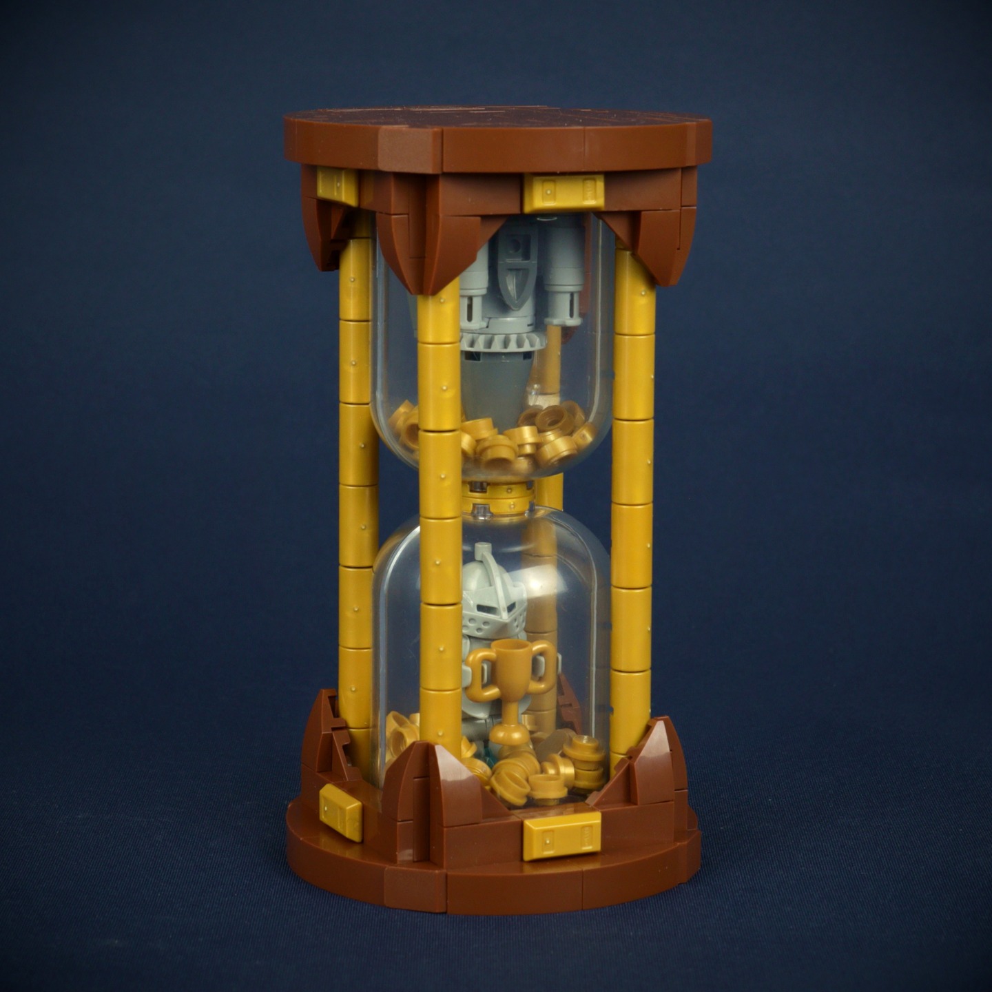 This hourglass is the official trophy for the 2025 Summer Joust 12x12 Vignette category!
The design of the trophy symbolizes the two dominant styles in vignette building: minifigure scale and microscale. The hourglass itself was chosen not only as a nod to its medieval origins, but also to reflect a key aspect of the challenge: the limited time builders have to create their entries. It's a tribute to the creativity and speed of those who rise to the occasion!
The trophy even includes a play feature! In between the golden studs you will find a diamond that can fit into the cup that is being held by the knight.
