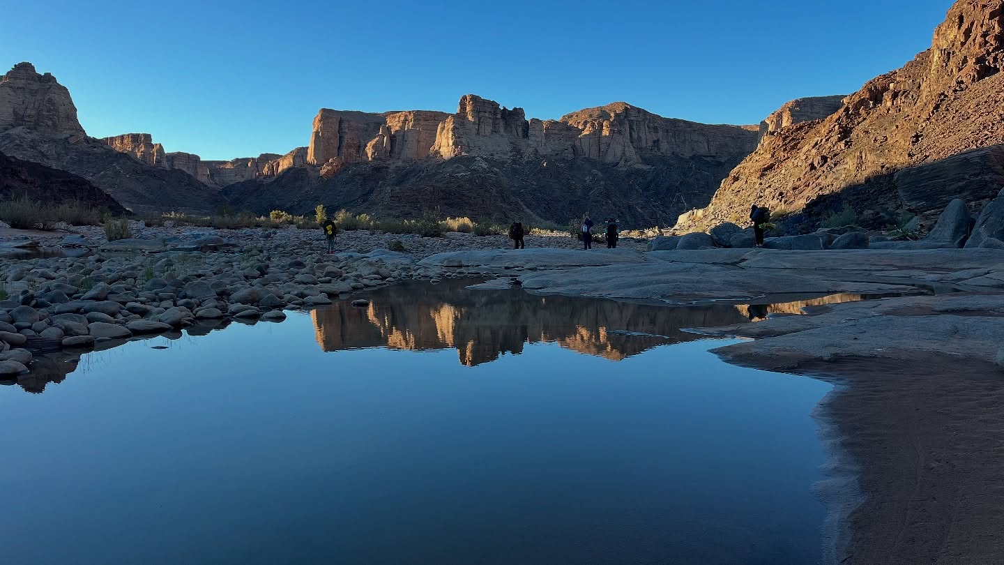 יום 6-7 - קו הסיום
הנחל כבר לא קניוני כמו בתחילתו. העיקולים רחבים ורדודים, ואפשר לראות את מפלס המים הנסוג. כמות המים בנחל תלך ותצטמצם עד השיטפונות בקיץ בשנה הבאה. גם אנחנו זורמים הלאה, מדשדשים בחול הרך ורוצים כבר להגיע ליעד –Ai Ais. אי אייס הוא נווה מדבר קסום עם מעיינות חמים, סביבם נבנה מתחם נופש. למרבה הצער, היום זה עוד אתר מבוזבז של רשות שמורות הטבע הנמיבית, שסובל מהזנחה ומחוסר חזון תכנוני משווע. מה כן יש כאן? מלון תמוהה משהו אבל נוח, בירה קרה והמבורגר אש! וגם קמפ סייט מקסים בטבע, גישה לנחל ובריכה עם מי הנחל החמים. עוד לפני הצהרים הגענו לכאן בתחושת הישג לא מבוטל, מלווה בעייפות שרירים ושלפוחיות של מסע כומתה. צוות המלון מצלצל בפעמון לבשר על הגעתנו, והנופשים מוחאים כפיים בהשתתפות בשמחה שלנו. עוד מסע תם. האם נחזור שוב?