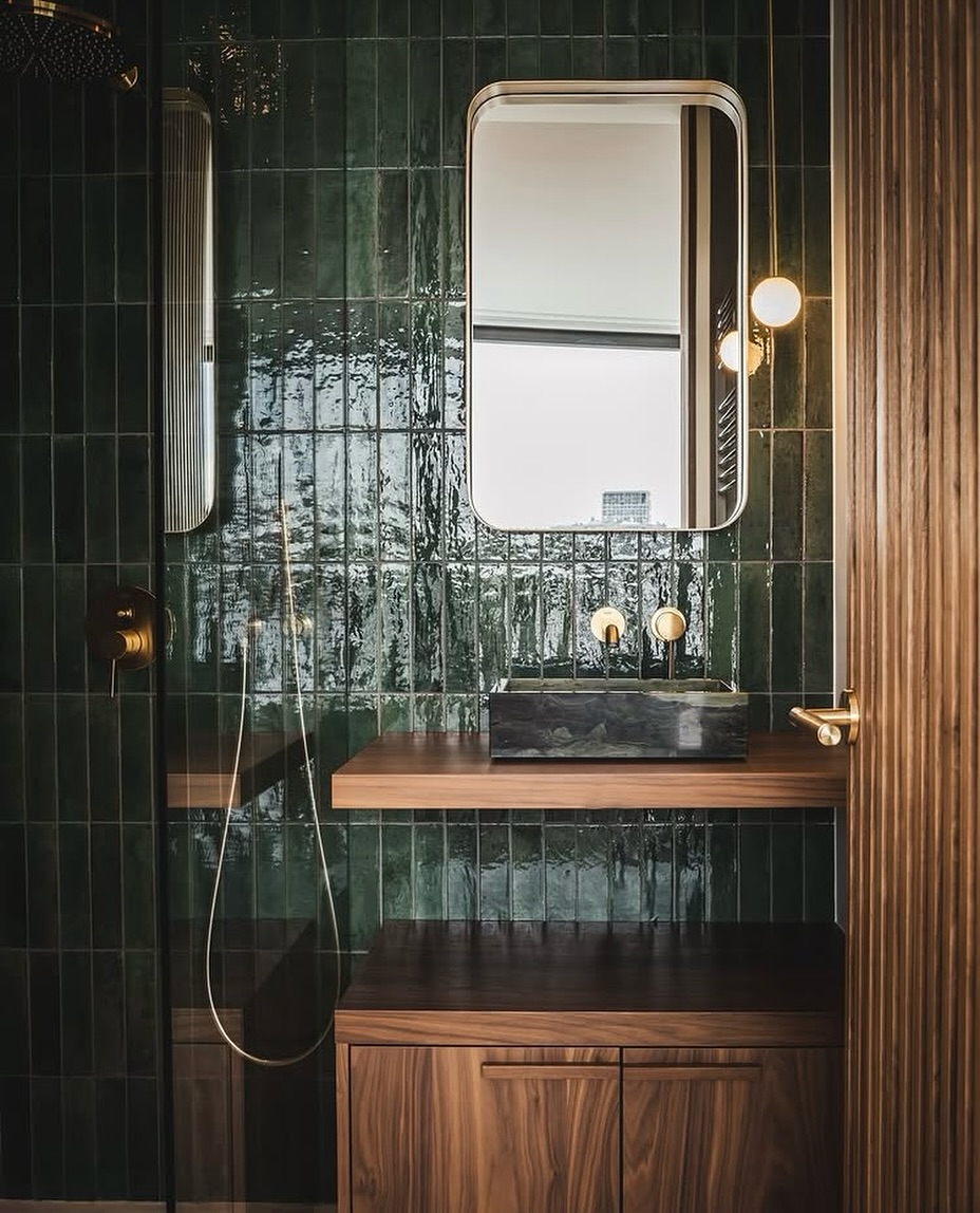 We paired deep green glazed tiles with warm walnut cabinetry, a sleek floating vanity, and a bold stone basin to create a space that feels both earthy and luxurious. Brass accents and soft lighting complete the look, balancing sophistication with comfort.
.
.
.
.
.
.
#tilesinspiration #luxuryinteriors #interiorinspiration #tegelsinspiratie #badkamerinspiratie #highendinterior #interiordesign #furniturespecialists #interiordesigner #residentialdesign #tiles #bathroominspiration #walnut #walnutfurniture #stijlvolwonen