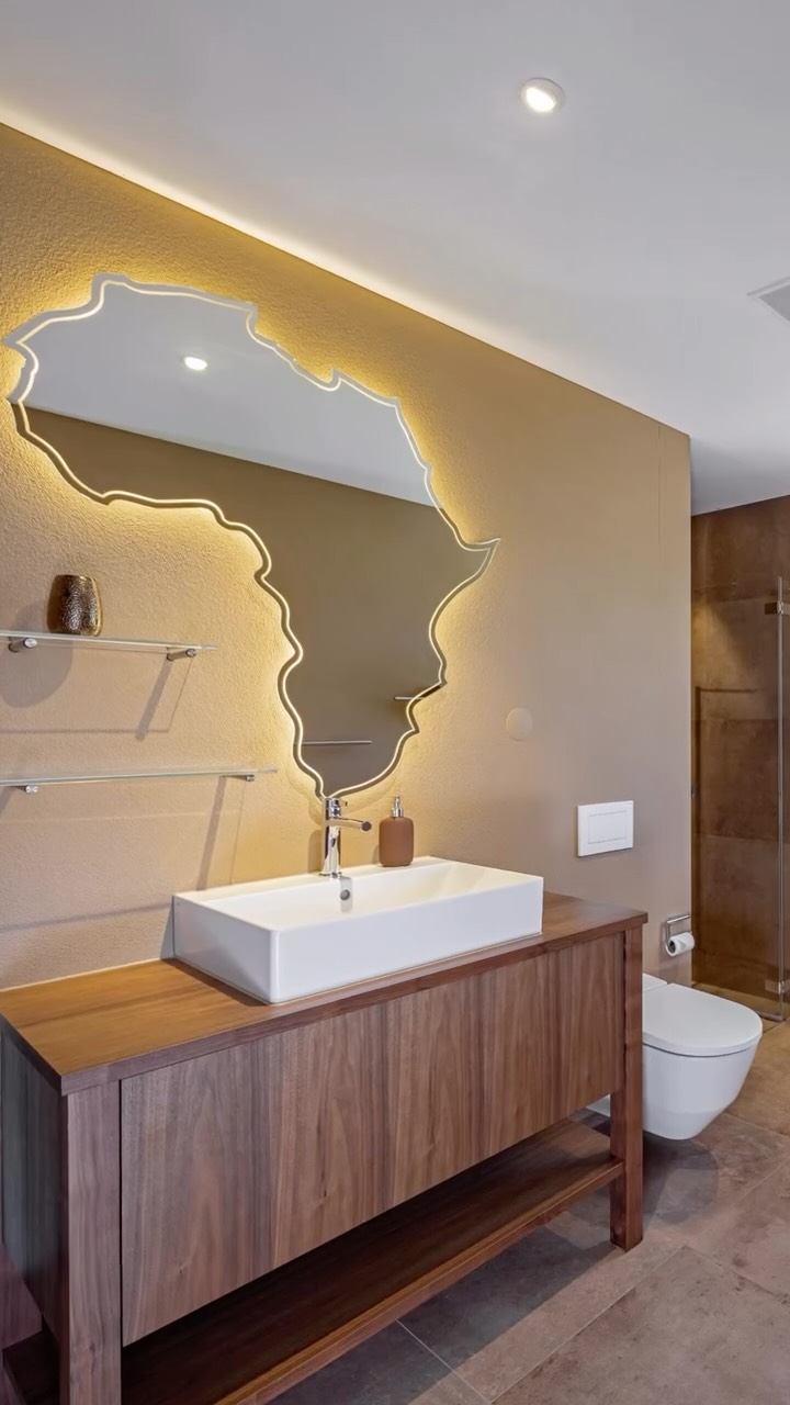 Ein Bad, das mit warmen Tönen Ruhe ausstrahlt.
Ein Spiegel in Form von Afrika, der zum Blickfang wird. Ein Innenausbau, der Schränke, Kommoden und Boden in einer klaren Linie verbindet.
Dieses Projekt zeigt, wie Persönlichkeit und Handwerk zusammen ein Zuhause prägen können.
