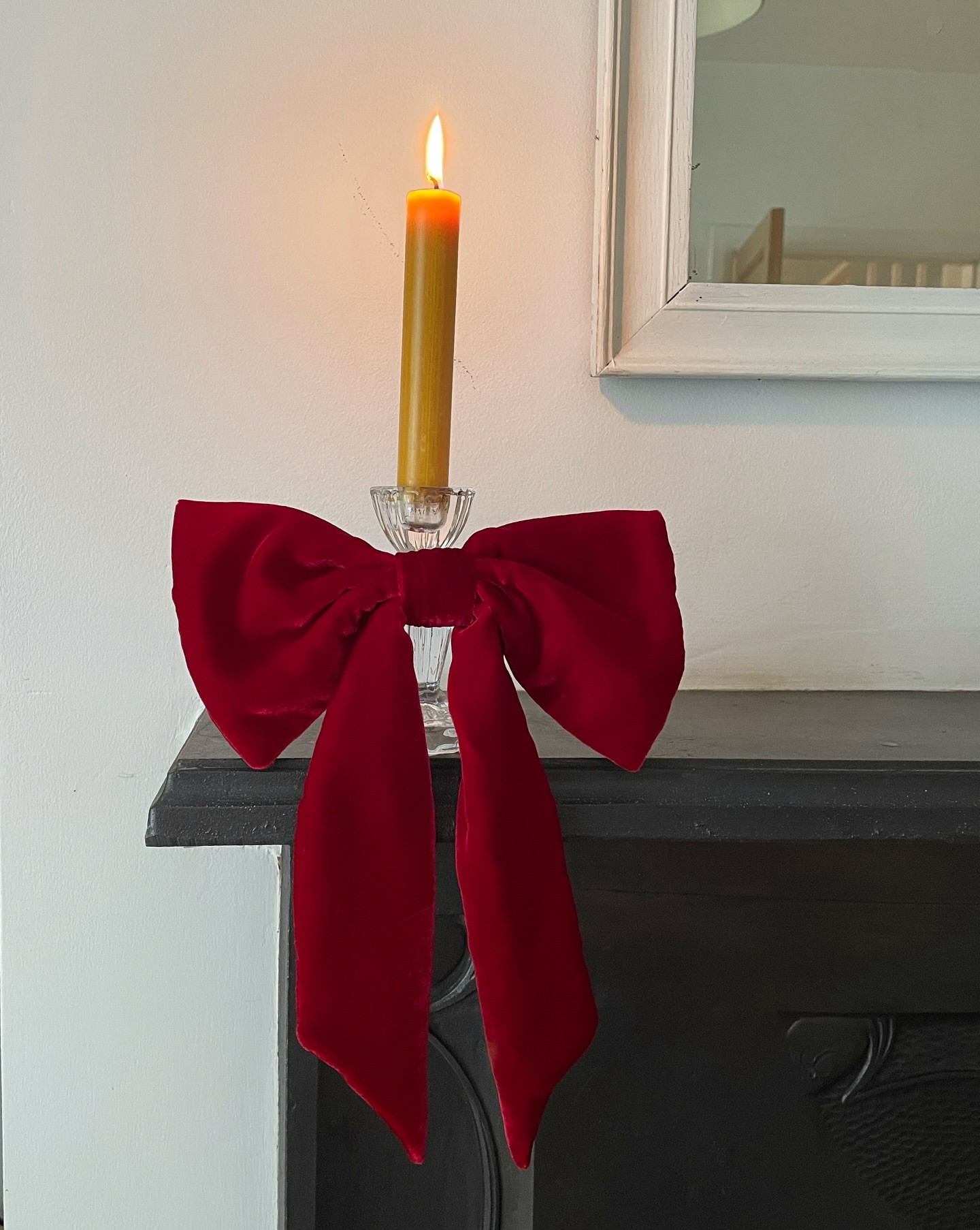 Now summer is gone and it’s October, can I start some festive hints?! So here is a peek of something I’m hoping to launch for winter with a photo I took in…July 😅
Image description- a red silk velvet bow around a glass candle holder with lit gold taper candle on a black mantlepiece