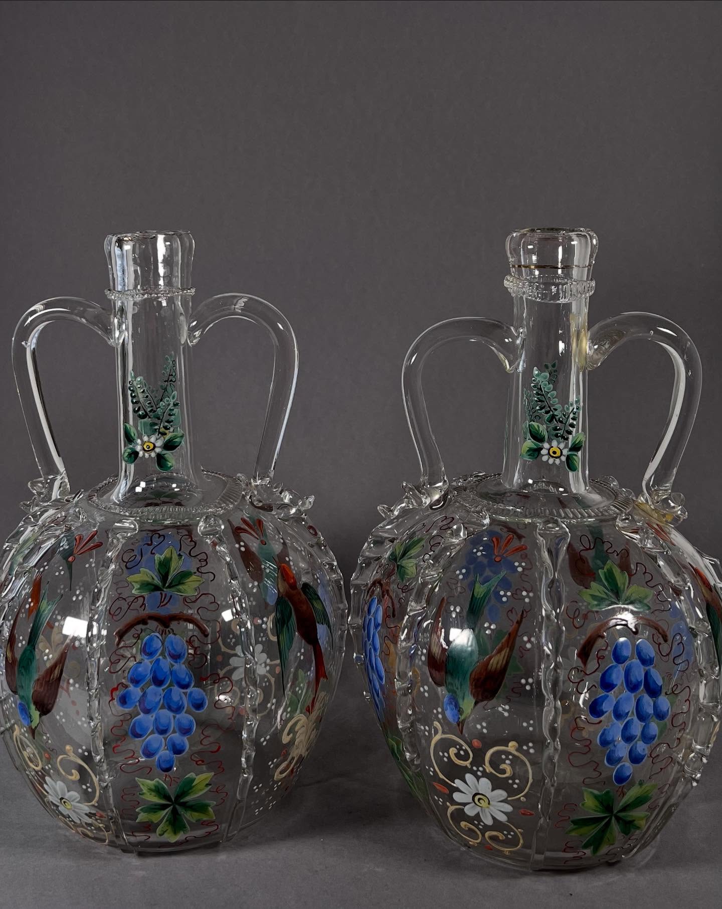 Glashütte Fritz Heckert (Petersdorf), um 1880–1890
Paar Doppelhenkelkaraffen – sogenannte „holländische Brautkaraffen“
Diese beiden kunstvoll gearbeiteten Gefäße knüpfen an historische Doppelhenkelformen aus den Niederlanden an, die seit dem 17. Jahrhundert bei Hochzeiten als symbolische Geschenke, Mitgiftstücke oder Repräsentationsobjekte eingesetzt wurden. Solche Karaffen wurden teils zur Vermählung befüllt überreicht, teils als sichtbares Zeichen von Wohlstand und Familienbindung im Haus aufbewahrt.
Der kugelige Korpus aus farblosem Glas wird durch zwei angesetzte Henkel und aufgelegte, gekniffene Glasstränge akzentuiert – typisch für die qualitätsvolle Fertigung der Glashütte Fritz Heckert. Die polychrome Emaillemalerei mit Weinreben, Vögeln und vegetabilen Motiven verweist auf Bildthemen wie Gemeinschaft, Fruchtbarkeit und Wohlstand. In der Verbindung von freigeformter Glasapplikation und fein ausgeführter Malerei zeigt sich die hohe dekorative und technische Kompetenz der späten Heckert-Produktion.
Maße:
Höhe ca. 25 cm
Durchmesser ca. 15 cm
Zustand:
– Eine Karaffe mit angesetztem, restauriertem Henkel und leichten Bestoßungen
– Zweite Karaffe mit Fehlstelle an den aufgelegten Glasfäden
Vergleich:
Fritz Heckert, Petersdorf, Form 387 (vgl. S. Zelasko: Fritz Heckert 1866–1923, S. 274)
Optionale Hashtags:
#FritzHeckert #HistorischesGlas #Brautkaraffe #Emaillemalerei #Glaskunst #Petersdorf #Kunsthandwerk #19Jahrhundert #DecorativeArts #Museal #Sammlerstück #Kulturgeschichte #AntikesGlas #Kunstgewerbe