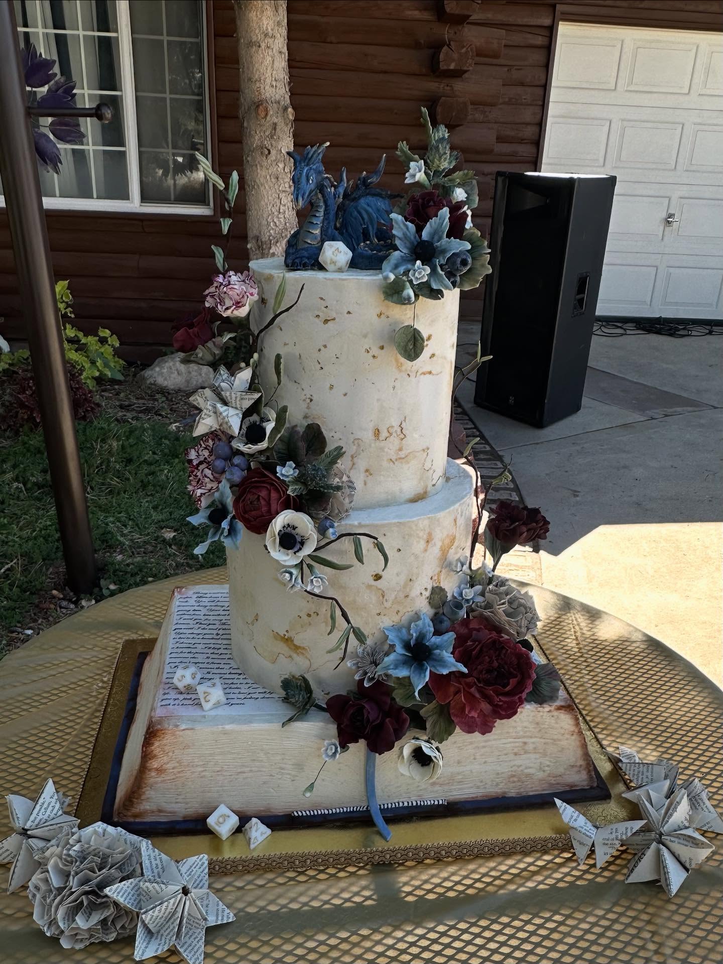 Dungeon & Dragons Themed Wedding Cake
When this couple came to me wanting an elegant but fantasy inspired cake with a nod to dungeons and dragons for their wedding cake, I had a bunch of ideas running through my head. We eventually decided on this design. The flowers are all handmade and made from sugar paste, we also incorporated paper flowers from storybook pages that the bride and groom were using as part of their decor. The dragon is hand sculpted and painted using modeling chocolate and edible lustre dust. The dice are make using @simisugarcompany isomalt
I had so much fun creating this one of a kind cake for this special couple.
Cake insides: Top-cookies and cream, middle-cookie dough lovers, bottom/book-strawberries and cream.
#dungeonsanddragonscake #dungeonsanddragonswedding #themedwedding #utahsugarartist #utahcakeartist