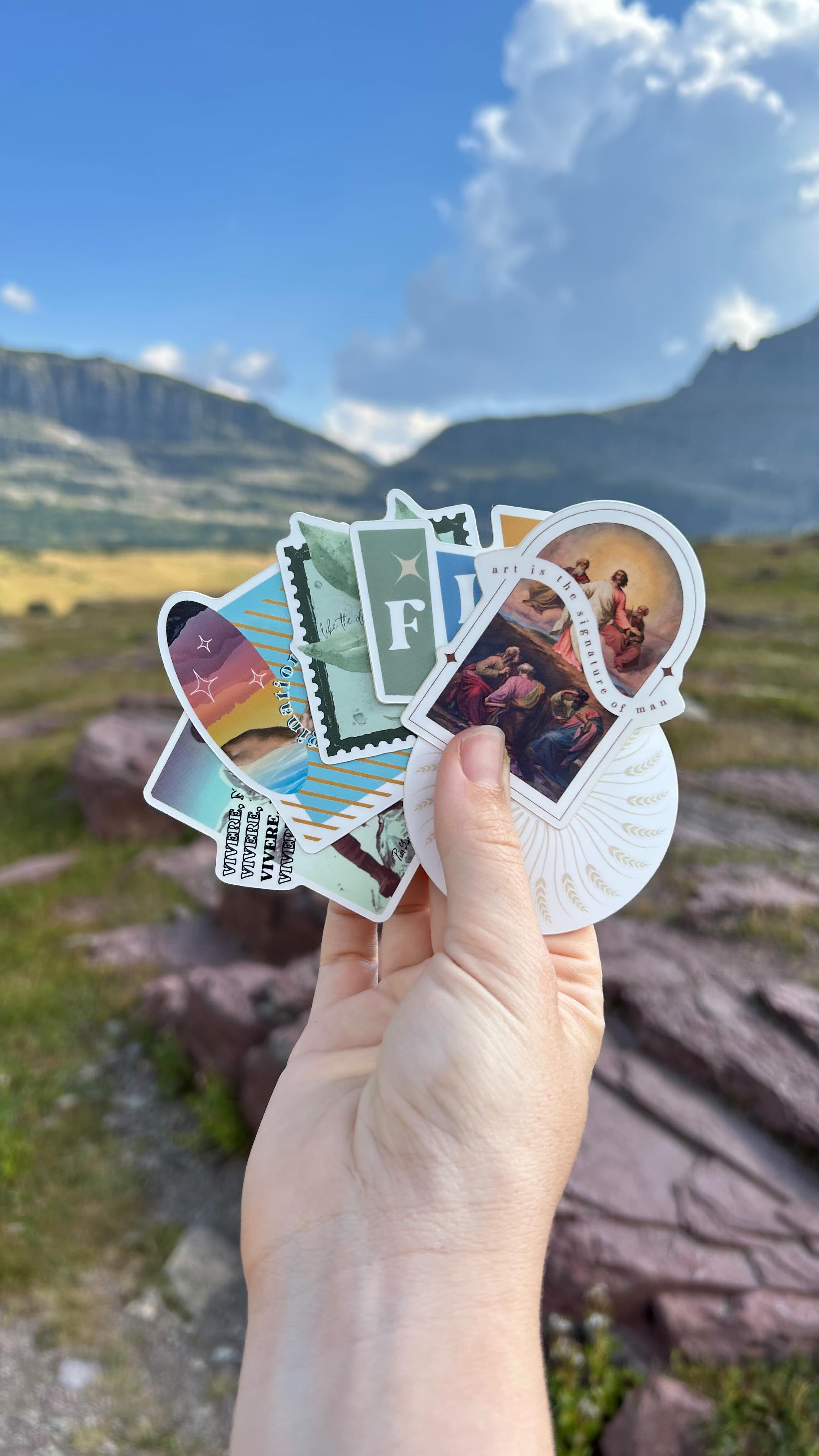 We’ve been working on a couple of exciting projects these past few months — from Frassati to Fiat and a whole lot in between — and we loved the designs so much that we turned several of them into stickers, packed them into our camper van and took them for a hike in Glacier National Park!
We’re working on getting a little mini shop up and running so we can get these stickers into your hands soon. Thanks for being along for the ride, we can’t wait to dive into the meaning behind the designs, perhaps we’ll make a series of posts in the coming weeks!
This past year of building this business, launching it and taking on new clients has truly been a dream. But the absolute very best part is the space this business has made for us to nosedive into art and beauty and creativity. Cultivating designs behind the scenes and then bringing them to life has truly been an absolutely enthralling and sacred endeavor. We are so grateful to get to do this. 😌🤍 Co-creatorship is absolutely the endeavor of a lifetime 🤌🏼