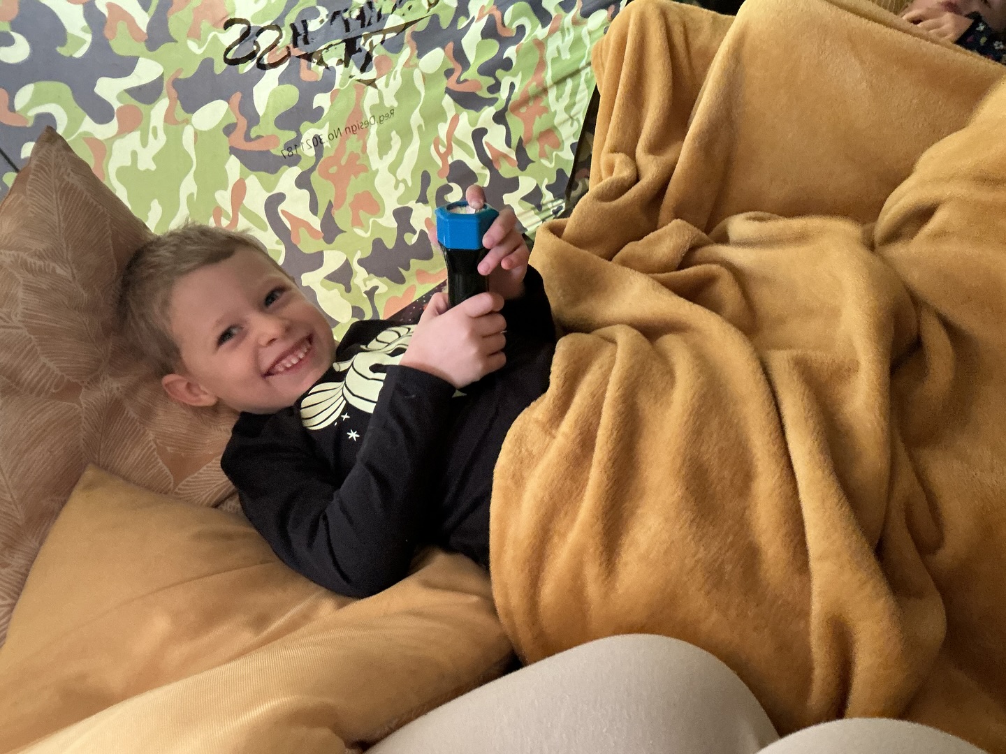 The Pre-School children created their own little camp in our camouflage tent today! Complete with blankets, pillows, torches and plenty of giggles! They shared stories, had a pretend sleepover, and enjoyed the calm, comforting feeling of being tucked up together.
These kinds of moments support so many areas of learning within the EYFS, from communication and language as they retell and invent stories, to personal, social and emotional development as they take turns, share space, and comfort one another. Even holding and shining the torches encourages fine motor skills and curiosity about light and shadow.
This also incorporates our Hygge ethos, soft lighting, close friendships, and the simple joy of feeling safe, warm and together. 🌿✨⛺