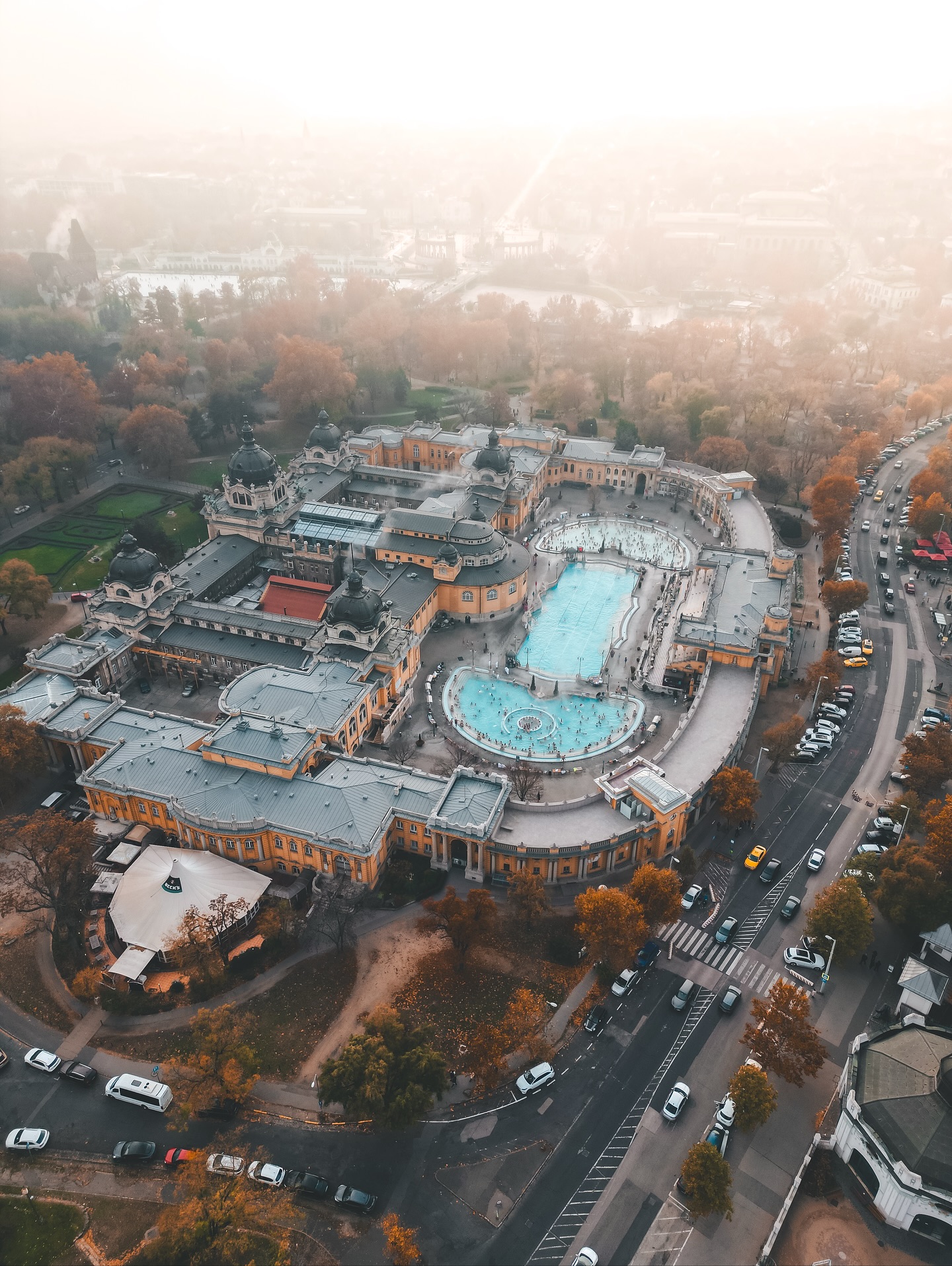 Budapest im Herbst hat diese Stimmung, bei der die Stadt in warmen Farben glüht und der Dampf über den Thermalbecken wie Nebel über einem See tanzt. Genau dann lohnt sich ein Besuch in der Szechenyi-Therme am meisten. Wenn draußen die Luft kühl wird und Ihr im heißen Wasser sitzt, fühlt sich das an, als würde die Zeit kurz stehen bleiben. Um Euch herum spielen ältere Herren Schach im Wasser, während Touristen versuchen, den perfekten Drohnenshot über dem gelb leuchtenden Gebäude zu erwischen. Es riecht leicht nach Schwefel, die Stimmen hallen leise zwischen den Säulen, und alles wirkt irgendwie entschleunigt.
Das Thermalwasser hier kommt aus zwei natürlichen Quellen, mit Temperaturen bis zu 38 Grad. Die Szechenyi-Therme ist eine der größten Anlagen Europas (15 Innen- und 3 Außenbecken), dazu Saunen, Dampfbäder und Massageräume. Aber ehrlich gesagt: Das wahre Erlebnis ist draußen. Im heißen Wasser sitzen, während die Herbstblätter fallen, ist fast schon ein Ritual in Budapest.
Falls Ihr nach dem Baden Hunger bekommt: Direkt nebenan im Stadtwäldchen gibt’s kleine Cafés, Langos-Stände und einen Blick auf das Vajdahunyad-Schloss. Ein idealer Tagesausklang.
#budapest #szechenyibath #szechenyithermalbath #thermalbath #budapesttravel #visitbudapest #hungarytravel #travelphotography #dronephotography #autumnvibes #fokusfernweh #reiseblog #europareise #thermalspa #travelinspo #europevacation #budapestcity #bathingculture #travelblogger #budapestguide #thermalexperience #wanderlust #bucketlisttravel #architecturelovers