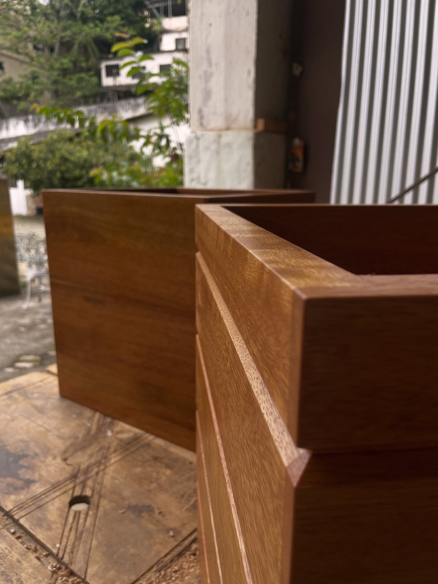 Nesse projeto, o cliente buscava um cachepô exatamente do jeito que imaginava e, como não encontrou nada parecido nas lojas, veio até mim com uma lista clara do que queria e do que não queria.
A partir dessas referências, desenvolvi propostas de desenho e escolha de madeira alinhadas às necessidades dele. Personalização total.
Mesmo quando algo parece simples, em madeira maciça nada é fácil 😅... É preciso prever dilatação, resistência ao sol, umidade, acabamento, durabilidade, cores e valores. Cada decisão importa no resultado final.
Para esse projeto, escolhemos o cedro marinheiro, que atendia perfeitamente aos requisitos técnicos e estéticos. As fibras foram posicionadas horizontalmente, e o encaixe lateral foi pensado para ocultar a madeira de topo (ponto mais sensível à umidade) e garantir robustez, já que a peça não poderia ter fundo para manter o esquadro.
O acabamento foi feito com três demãos de stain, que penetra na madeira, protege contra os raios UV e realça toda a beleza natural do cedro.
O resultado: dois cachepô resistentes, um liso e um com rasgo, bem pensados e bonitos. Exatamente como o cliente imaginou. 🫡