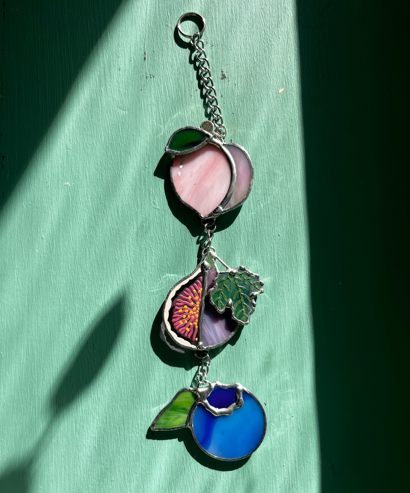 Loving this dramatic lighting that was going on for these pics 😂 another little fruit chain - we call this one the bisexual fruit chain, with its subtle bi flag colors. Of course the fig is the star of the show here, painted to perfection by @glass.creature 🩷💜💙