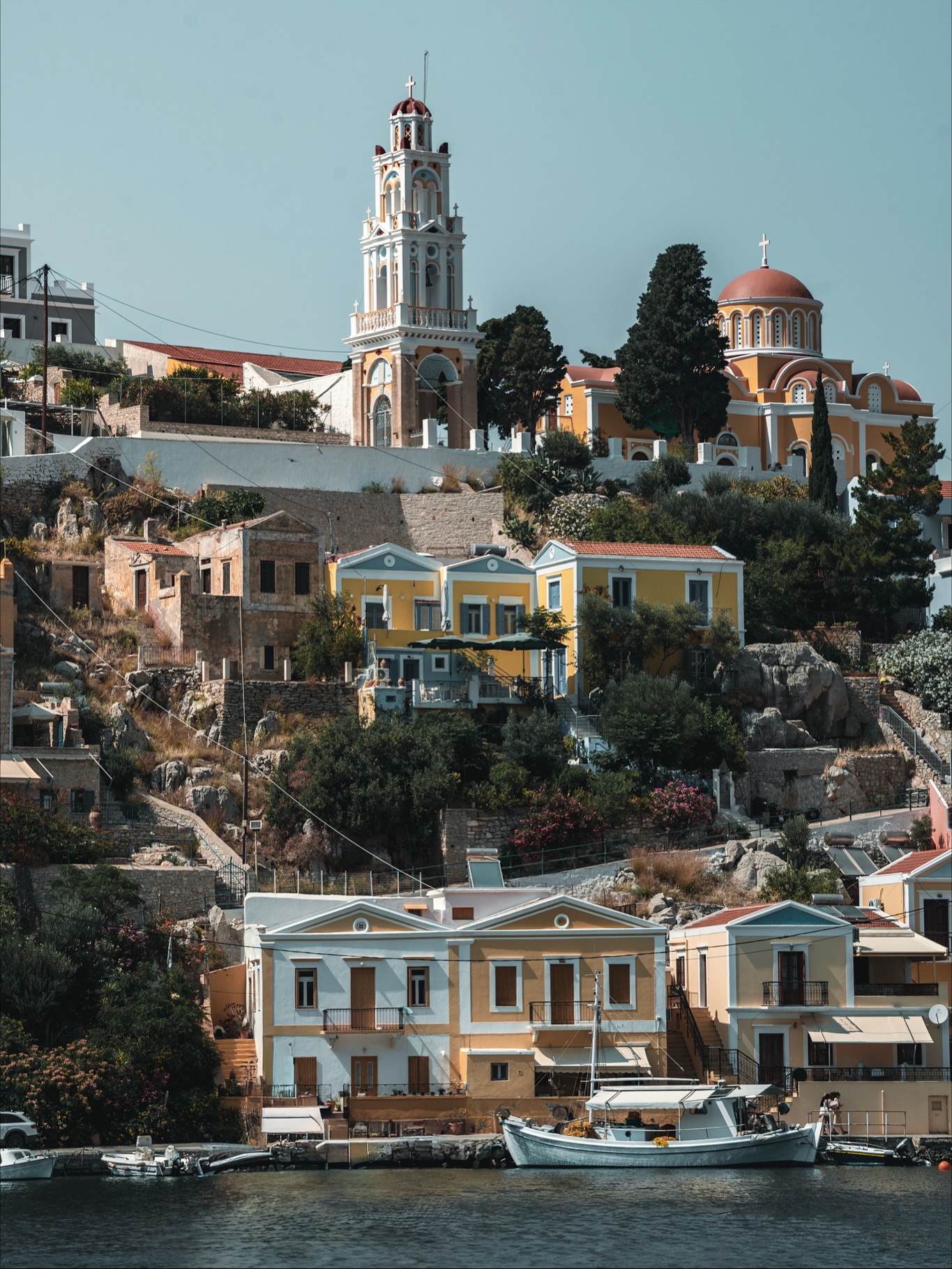 Symi ist so ein Ort, der sich anfühlt, als hätte jemand eine ganze Farbpalette über die Hänge gekippt und gesagt: passt schon, wird schön. Und genau so sieht es dann auch aus. Terrassen aus kleinen Häusern, die sich übereinander stapeln, Boote, die gemächlich im Wasser dümpeln, Gassen, die nach Sonne, Salz und einem langen Mittag riechen. Ich laufe da rum und frage mich ständig, wie oft diese Türen wohl neu gestrichen werden, damit sie so satt aussehen. Und wie man es hier schafft, nicht permanent die Kamera im Anschlag zu haben.
Zwischen den Restaurants sitzen Menschen im Schatten, während ein paar Meter weiter die Fischerboote an ihren Leinen schaukeln. Über mir die Kirche, weiter oben der kahle Hang, der fast schon wie ein natürlicher Rahmen wirkt. Und unten am Hafen passiert alles gleichzeitig und irgendwie auch nichts. Boote legen an, Händler rollen Körbe mit Schwämmen raus, Katzen streichen durch die Tische. Jeder Winkel schreit danach, festgehalten zu werden.
Ich mag diese Orte, an denen die Kulisse wirkt, als hätte sie jemand für eine Postkarte geplant, aber man trotzdem echte Momente erwischt. Ein Mann am Wasser, der sein Boot putzt. Menschen, die im Café lachen. Eine Tür, hinter der jemand gerade Mittag macht. Und mittendrin ich, der versucht, nicht dauernd stehen zu bleiben, weil der nächste Blick schon wieder besser ist als der vorherige.
#symi #greece #visitgreece #harbourlife #islandvibes #travelgreece #greekislands #mediterranean #travelling #fokusfernweh #photography #streetphotography #islandphotography #dronephotography #reiseblogger #travelmoments #wanderlust #travelcouple #aroundtheworld #greekarchitecture #discovergreece #symiisland #travelcaptures #seasidevibes