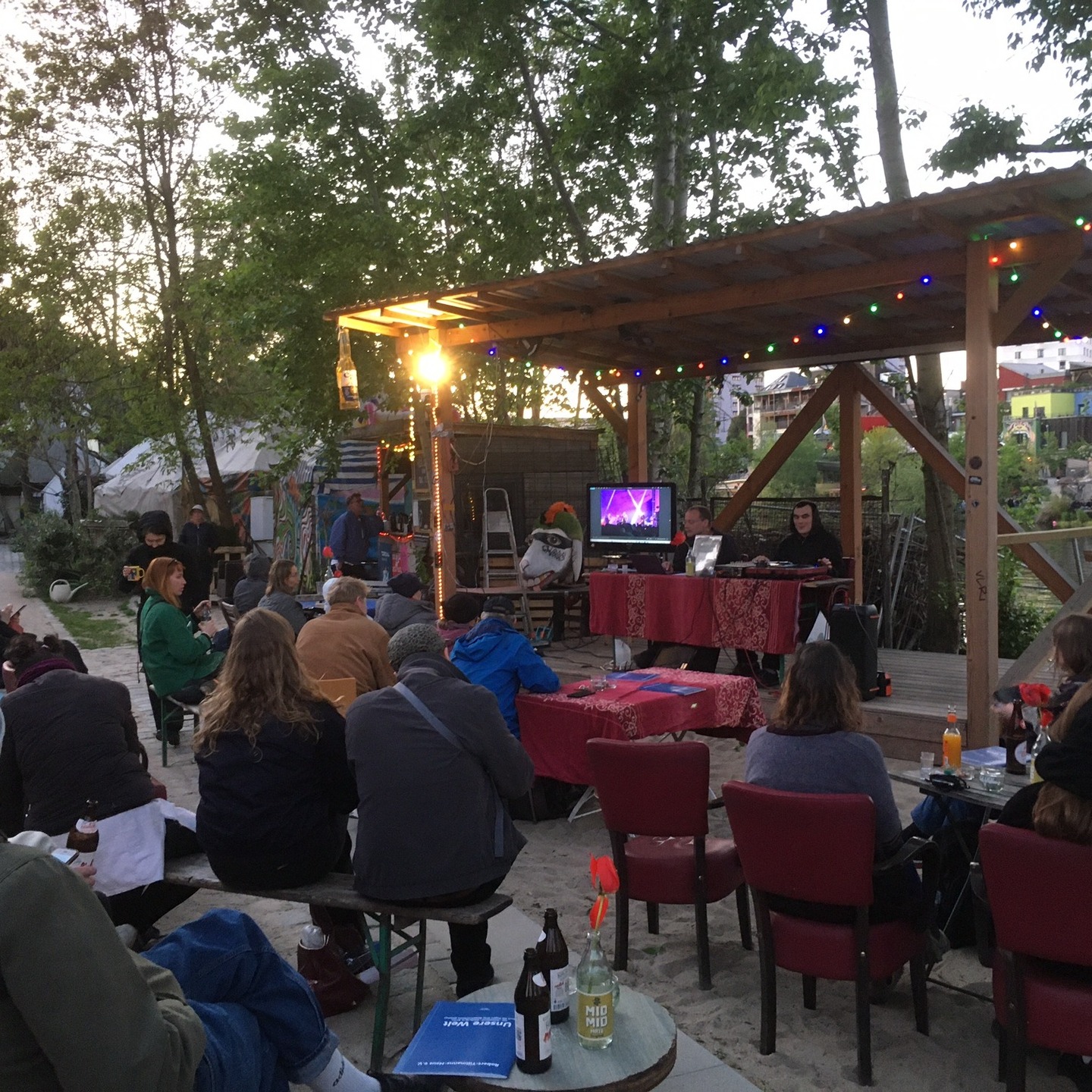 „Sound & Vision: Berlin Underground“
Bereits seit dem 19. Jahrhundert gilt Berlin als Hauptstadt dessen, was man seit den 1960ern als „Underground“ bezeichnet. Dabei geht es um politische, gesellschaftliche und kulturelle Prozesse/Ereignisse, die im Verborgenen stattfinden, da sie illegal oder geächtet sind oder die Akteure sich bewusst vom gesellschaftlichen Mainstream abgrenzen möchten. Der Betrachtung des Undergrounds stellt somit eine ganz eigene Form der Geschichtsschreibung dar, die die herkömmlichen Darstellungen um wichtige Aspekte ergänzen, sie zugleich aber auch fundamental in Frage stellen kann. Zugleich gehört die Underground-Kultur bis zum heutigen Tage zu den Faktoren, die vor allem jungen Menschen dazu bewegen, nach Berlin zu kommen.
Am 26.04. wurde dieses Thema ab 19 Uhr im Rahmen einer niedrigschwelligen Veranstaltung in der „Teepeeland“-Siedlung. thematisiert. Niko Rollmann zeigte dafür historische Photos/Graphiken, während der Musiker/Künstler Leon Baumgartl komplementäre Underground-Songs per Schallplatte abspielte. Im Ganzen wurden 18 Bilder gezeigt, unter anderem zu den Bereichen Prostitution im Kaiserreich und im gegenwärtigen Berlin, der sexuelle Untergrund der Ersten Weltkrieges, untergetauchte jüdische BerlinerInnen während des Zweiten Weltkrieges, Underground-Kultur im West-Berlin der späten sechziger Jahre, der queere Untergrund in West-Berlin in den siebziger Jahren, Punk-Bewegung in der DDR, „Obdachlosigkeits-Untergrund“ der 1990er. Die einzelnen Motive wurden jeweils in ihren historisch-politischen Kontext eingeordnet durch inhaltlich passende Musikstücke ergänzt. Zu Leons „Tracklist“ gehörten zum Beispi