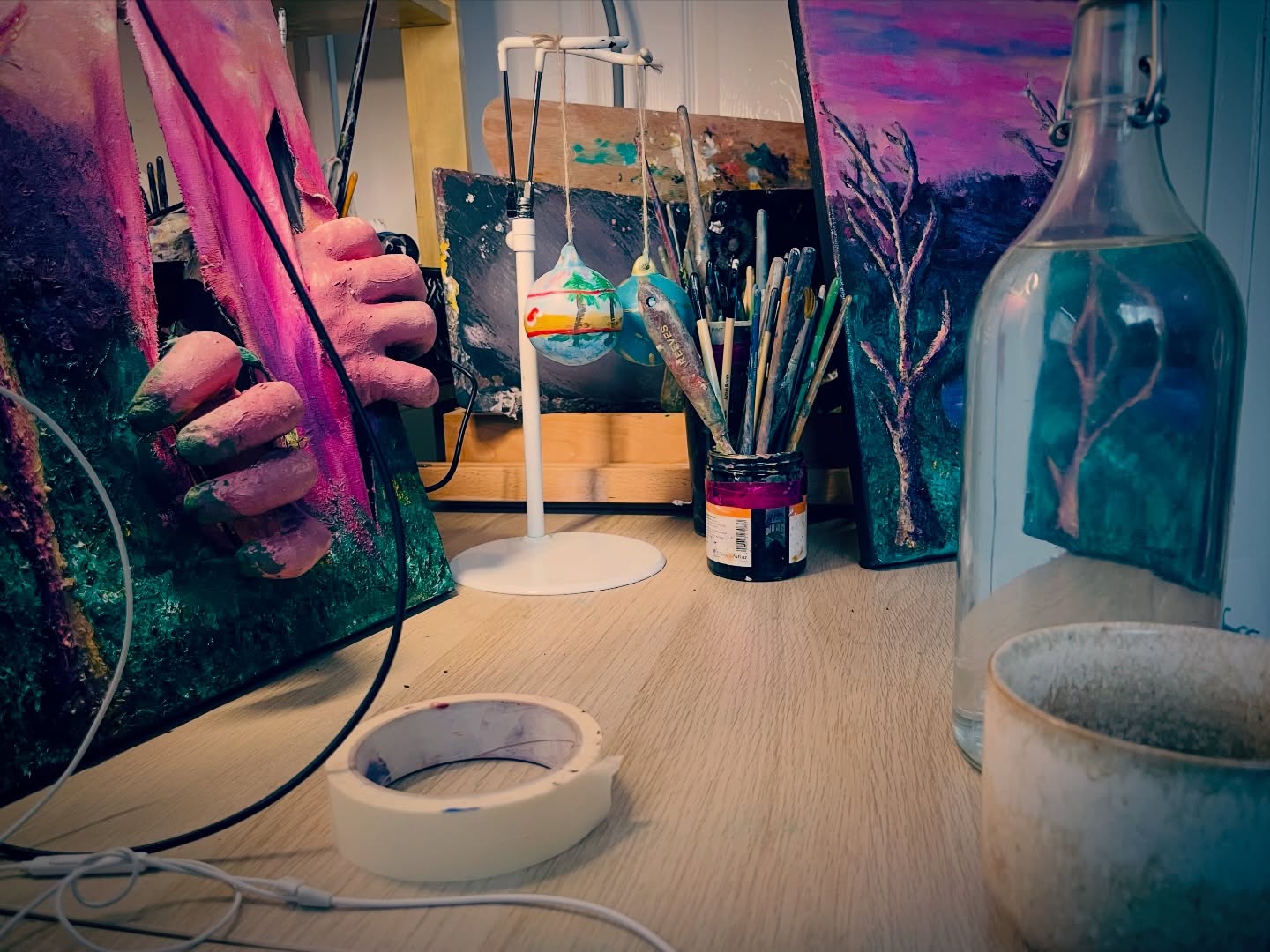 Brushes, colour palettes, easel, Christmas bulbs, masking tape, water, coffee and plaster cast hand braking through a canvas, isn’t this everyone’s work desk?