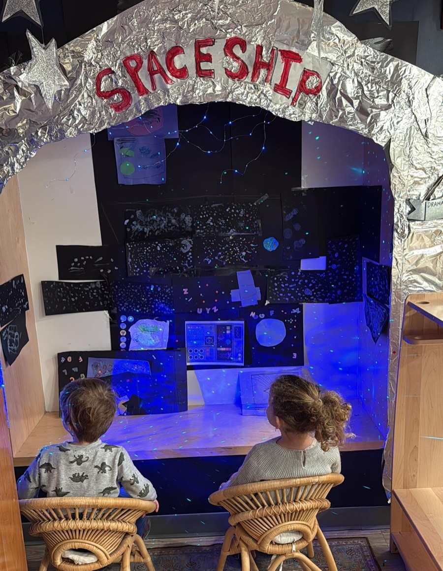 As part of our light and Chanukah theme, our Pre-K East friends transformed their dramatic playhouse into a spaceship! They started by painting stars on black paper with fine brushes to create our spaceship window view. This led to interesting discussions about the illusion of depth, with closer stars being painted as larger white dots and distant ones as smaller dots. A child shared her planetarium experience of seeing the Big Dipper, which prompted us to look it up and paint it together. Then, we focused on creating a control panel for the spaceship, using various materials like colored paper for screens and buttons, stickers, and recycled cardboard tubes for levers. #LearningToExplore #ExploringToLearn #ReggioClassroom #LearnThroughPlay