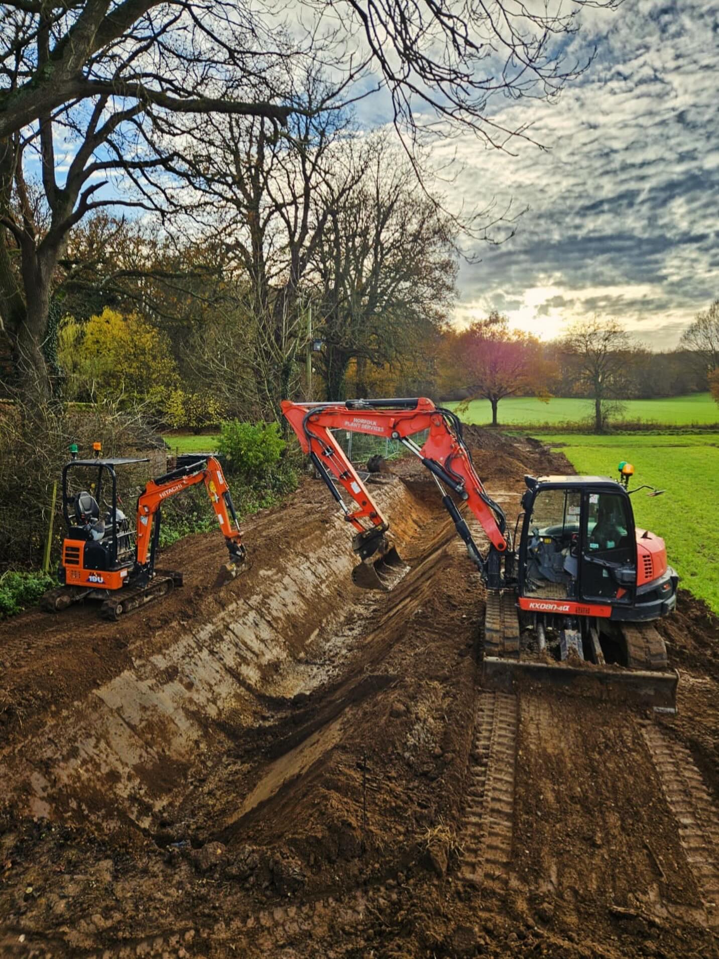 We do like a bit of warm orange plant on these wet cold days. These pair are working in tandem to excavate a swale to eliminate flooding risk.