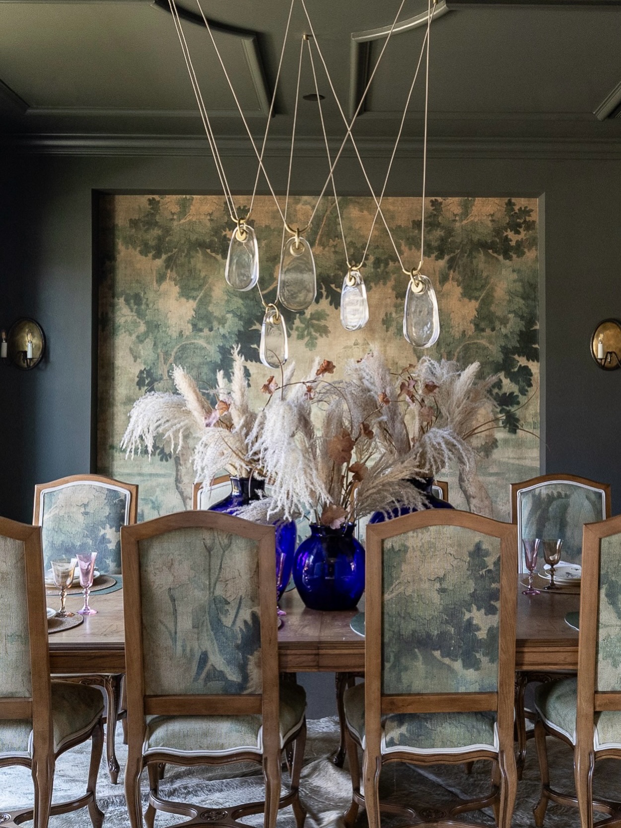 Some rooms beg you to slow down, and this one whispered from the very beginning.
I wanted this dining room to feel like a gathered moment, where history, texture, and a little bit of magic meet in the most effortless way. The moody walls wrap you in, the ceiling adds that quiet architectural drama, and then the mural… she became our muse.
We upholstered the vintage dining chairs in the same landscape pattern as the mural; a subtle, immersive layer that makes the whole room feel collected and softly storied. It’s one of my favorite ways to create cohesion without being too coordinated.
It’s a space meant for long dinners, candlelight, good conversation, and maybe a little lingering long after dessert.
Let us know what part you gravitate toward first〰️ the ceiling, the mural, the chairs, or the sculptural chandelier.
Builder: @southernserenityhomes
Photography: @jennifer.saltsman.photography