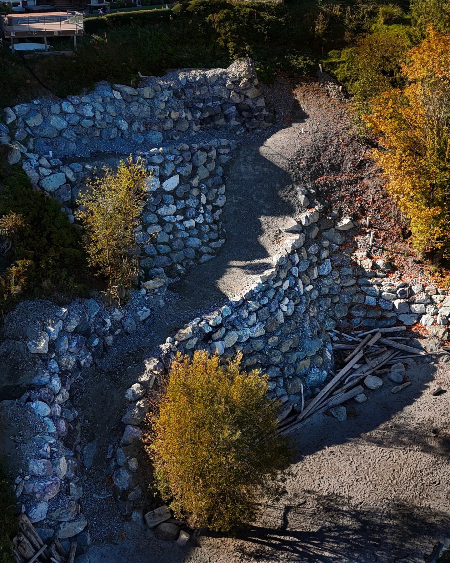 Shoreline Reclamation
If you didn’t know, one of our specialties is building sea walls to reclaim and protect coastal land.
This particular project was a true test of skill. Creating a boulder wall of this scale requires a massive amount of patience and a “finesse” touch with our Liebherr. The logistics were a puzzle in themselves; since we were working off a cliffside, everything moved by water. Every yard of soil we took out and every boulder we brought in happened via barge.
Beyond the aesthetics, safety was a huge priority. What started as a messy, sliding cliff of falling trees and loose soil is now a stable, and secured by an engineered wall. By locking down the shoreline, we’ve made the public beach below much safer for the community.
Seeing it finished, it’s more than just a retaining wall—it’s a piece of functional art that will stand the test of time, & and age like fine wine over time.