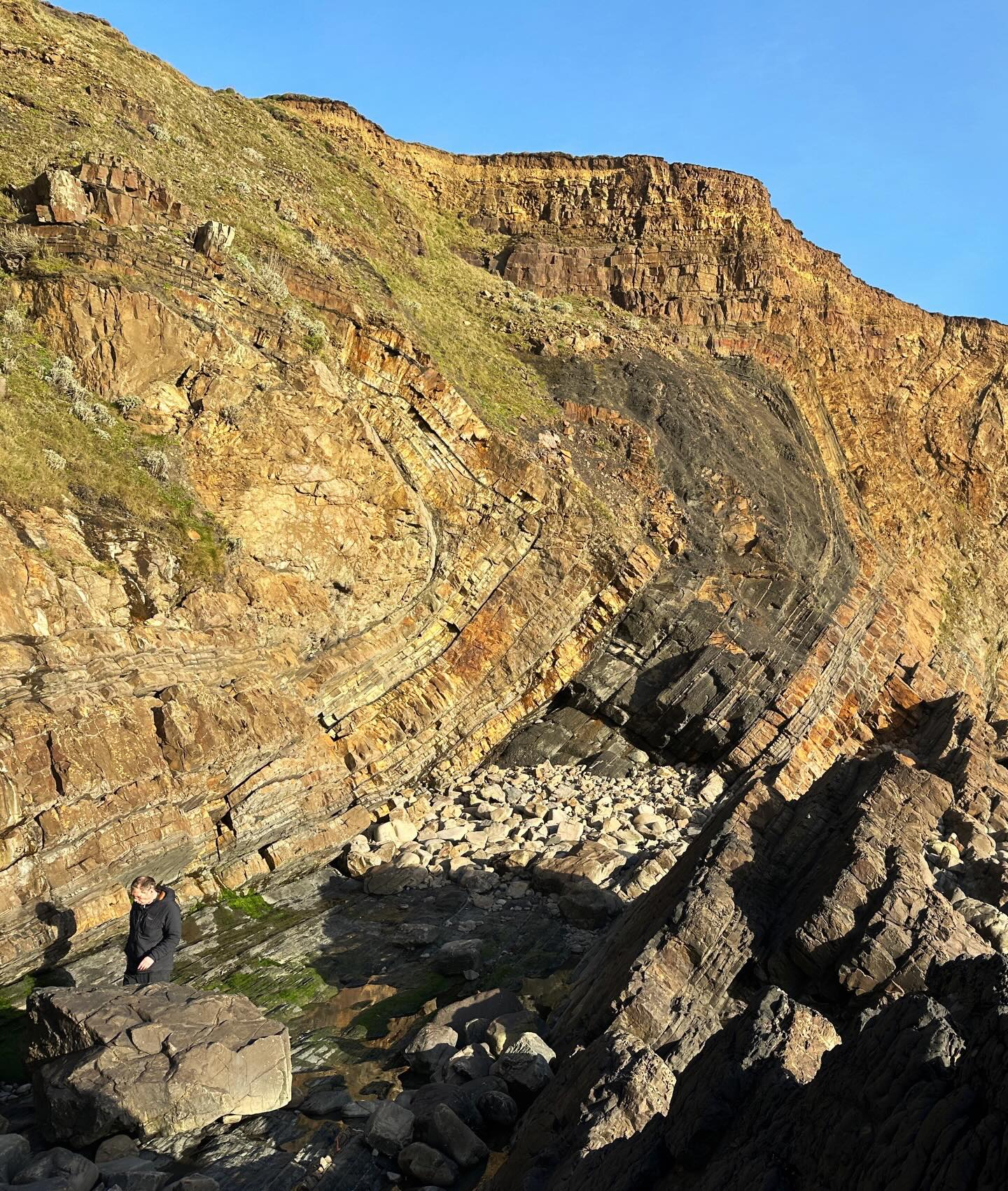 Folded flysch in North Cornwall.
Flysch is the traditional term for a broadly fining upwards sequence of sandstones and mudstones, deposited from turbidity currents (underwater avalanches) on submarine continental slopes.
The Bude Formation formed during syn-convergence sedimentation in the Culm Basin, and then subsequently buried and then inverted during the Variscan Orogeny. These rocks host some incredible sedimentary structures.
The Variscan folds here face southwards. Fold facing is the direction in which the beds get younger in the hinge of the fold. In this image it is left to right.
The southwards facing folds in this area are anomalous, contradicting the northwards transport direction of Variscan tectonics.
They occur because of the pre-Variscan faults that underly these units and controlled the formation of the Culm Basin. These faults towards the south end of the basin dip northwards. This dictated how strain was accommodated during inversion or the basin, with the expulsion of these sedimentary layers southwards.
The cliff height here is about 30 m.
#budeformation #flysch #widemouth #widemouthbay #cornwall #cornwallcoast #cornishcoast #cornwallgeology #cornishgeology #geology #geologyrocks #geolife #geologist #geologistsofinstagram #learninggeology #geoadventure #exploregeology #geologicalwonders #explorecornwall #walkingcornwall #lovecornwall #bbcspotlight #ordnancesurvey #structuralgeology #sedimentary #variscan #geologyfieldtrip #tectonic #tectonics #tectonicplates