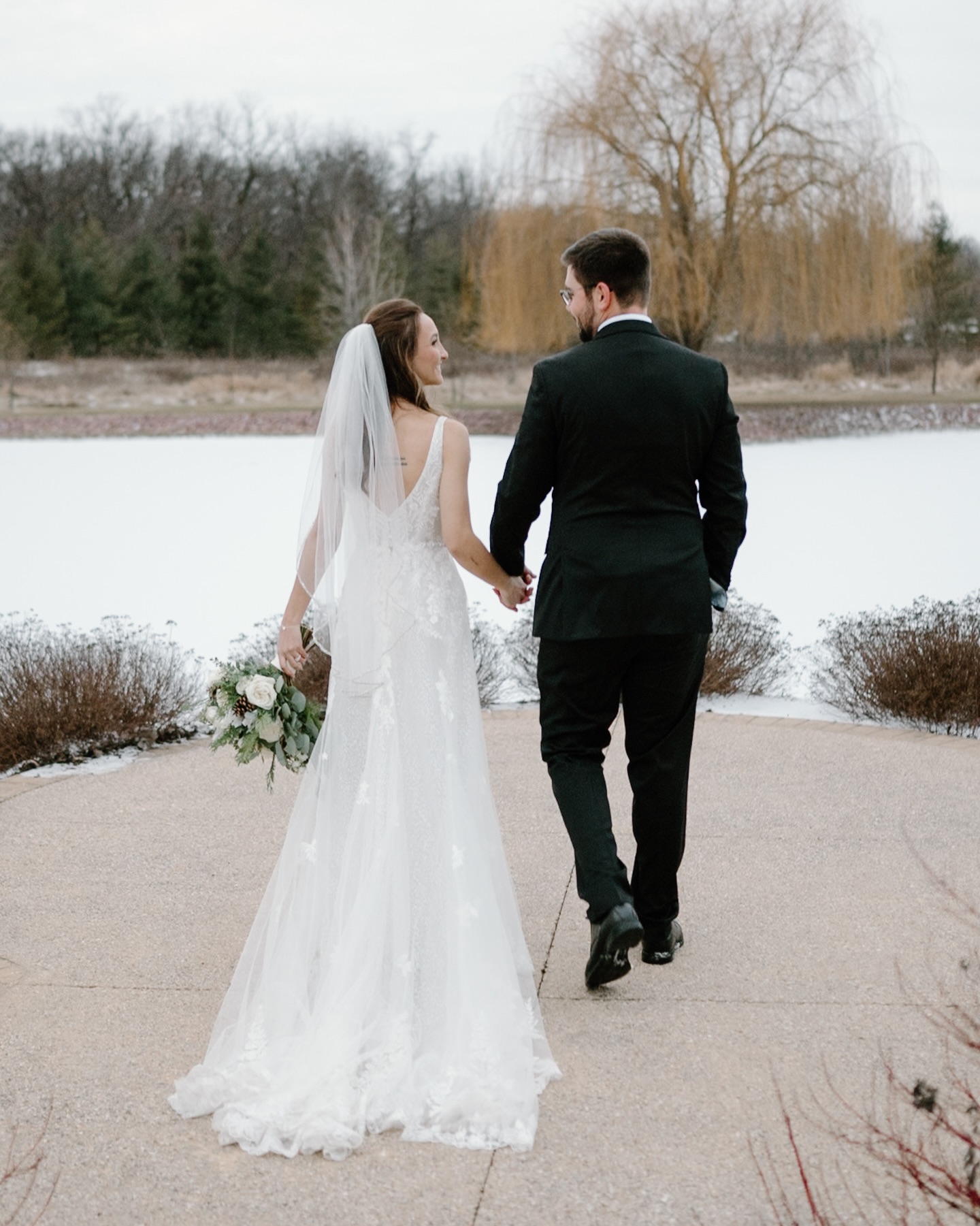 Would you plan a winter wonderland wedding? ❄️🌲
Just over the Wisconsin border in Rockton, Illinois is a hidden gem of a wedding venue: the Pavilion at Orchard Ridge. It was an exceptionally cold January day for Madeline and David’s Pavilion at Orchard Ridge Wedding. Madeline and David had their early January winter wedding at this beautiful barn wedding venue in the countryside in northern Illinois. There was a dusting of snow on the ground. The bridesmaids got ready at the Copperstone Inn, a beautiful inn on the property of the wedding venue. The bridesmaids dresses were a lovely pale green. The bride and groom chose winter decorations such as pine boughs and pine cones and white florals to decorate the venue. The pine in the floral arrangements smelled amazing! They even folded their reception napkins in a fun shape: a pine tree!
The bride and groom wrote letters to each other to read after their first touch. They chose to do a first touch instead of a first look. The couple had their ceremony indoors in the beautiful barn in front of the beautiful fireplace. The bride’s brother was the officiant and he played a prank on the bride by dressing up in a pope outfit when he entered for the wedding reception. Their vows were funny and emotional. The venue has windows that wrap around three sides of the barn that overlook a lovely pond and the countryside. There is a cute bridge over the pond with a willow tree in the background. The couple and their friends and family had a candlelit dinner followed by dancing.
Venue: Pavilion at Orchard Ridge
Photographer: Brianna Kraft Photography