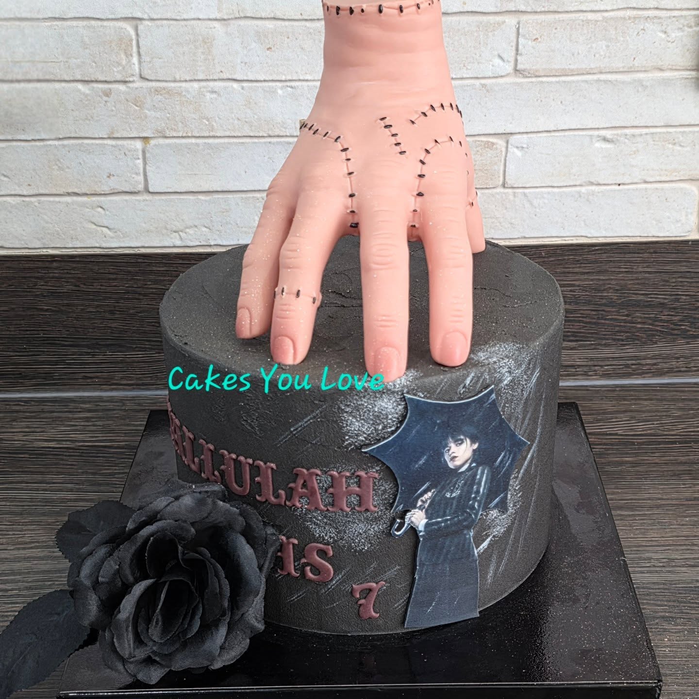 A Wednesday Adams themed cake. Thing is non edible. Wednesday is printed on icing and the rain added by hand