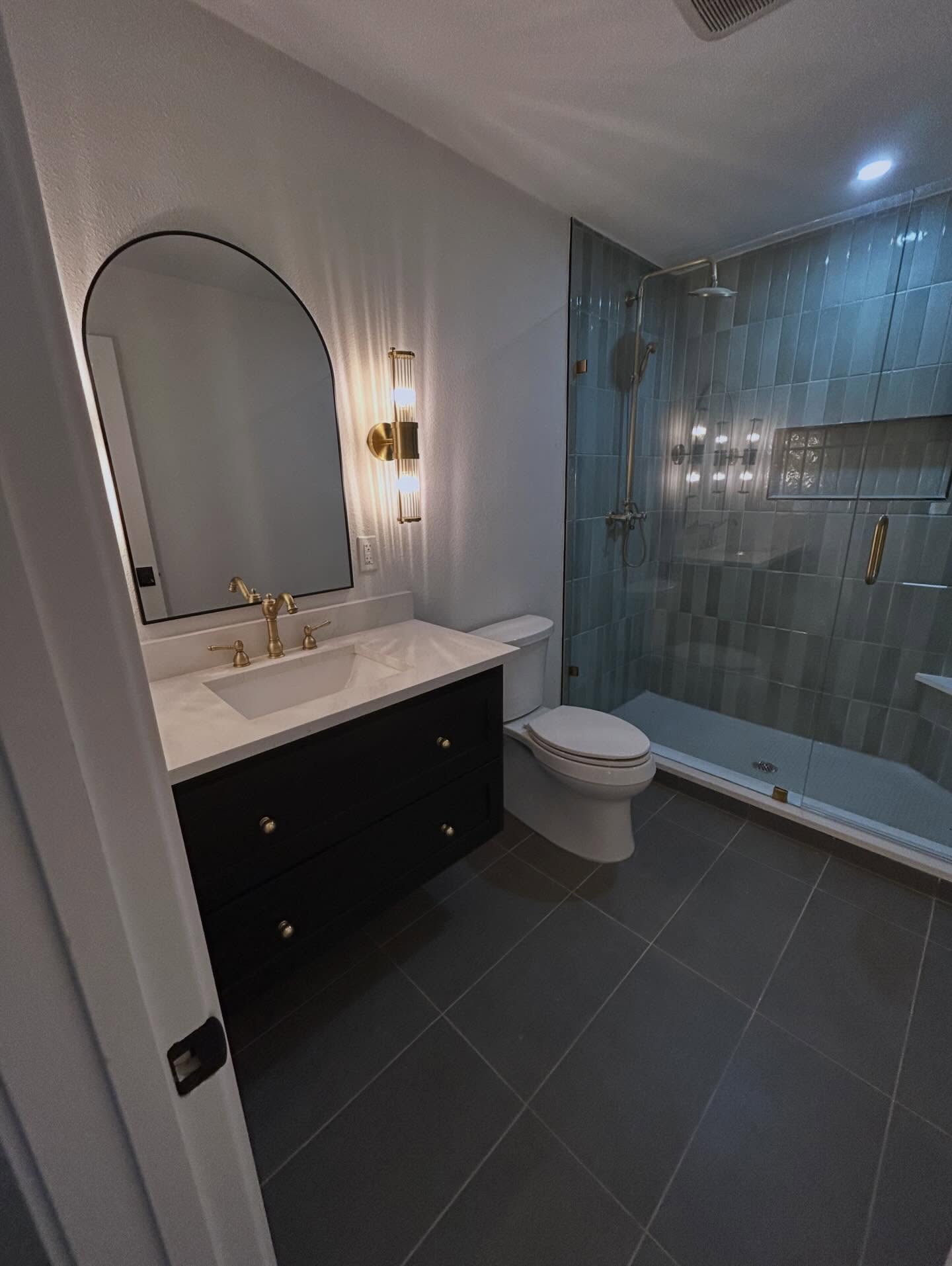 Proof that thoughtful design changes everything. Sleek shower tile, vanity, and lighting transform this space to be a show stopper! #dallasremodel #bathroomreno