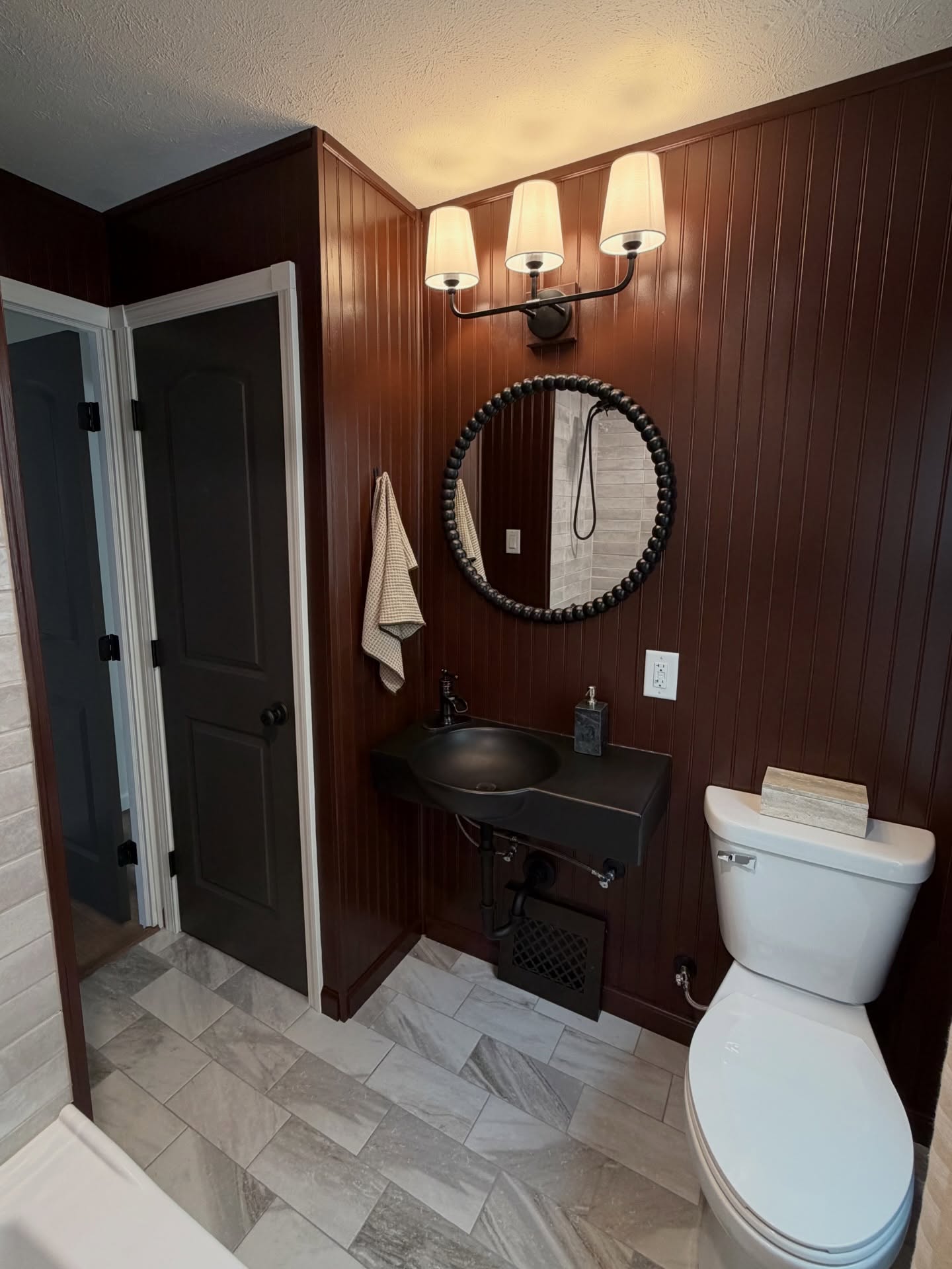 Rounding out the rest of the first floor with our full bathroom sharing a hall with 2 bedrooms! Perfect space for an office, children’s room or guest room
Statement bathroom featuring a deep bath, shower including a double niche and modern tile layout, floating honed black sink, deep burgundy beadboard walls, eclectic mirror and linen shade vanity light
Amazing mix of traditional richness and contemporary finishes