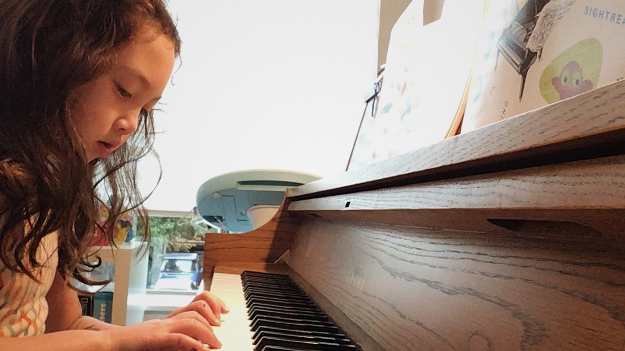 On days like this, I’m especially thankful for quiet rooms, steady notes, and the chance to play music with my students.
Image description: A child sits at an upright piano, focused on the keys as warm light fills the room around them.